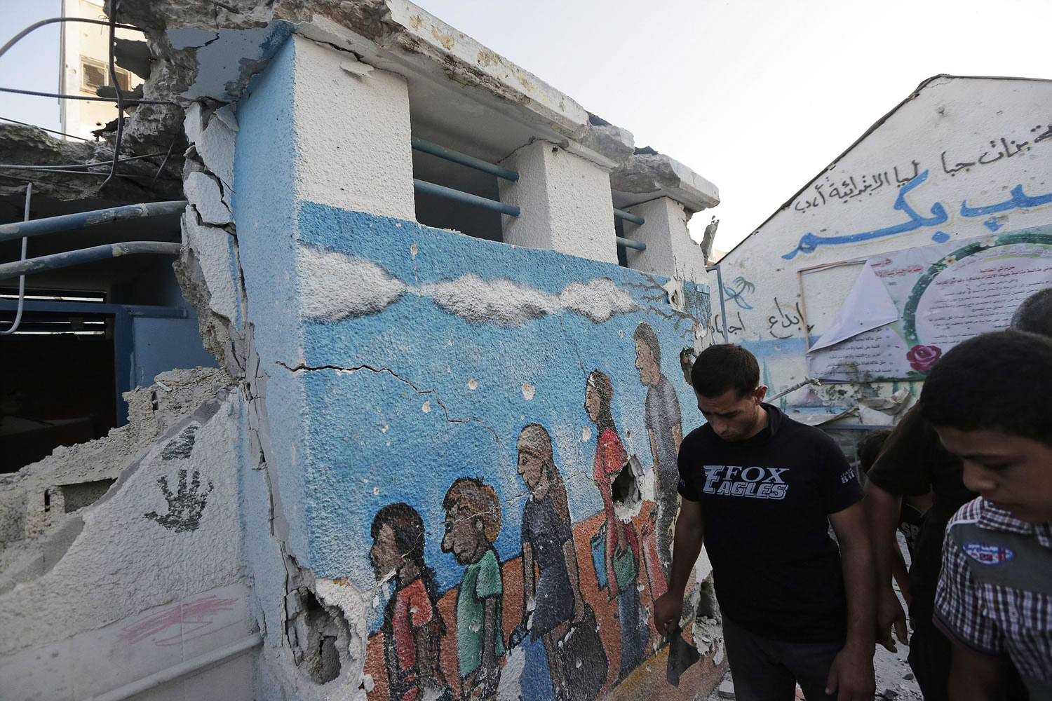 Palestinian walk by a damaged classroom at the Abu Hussein U.N.