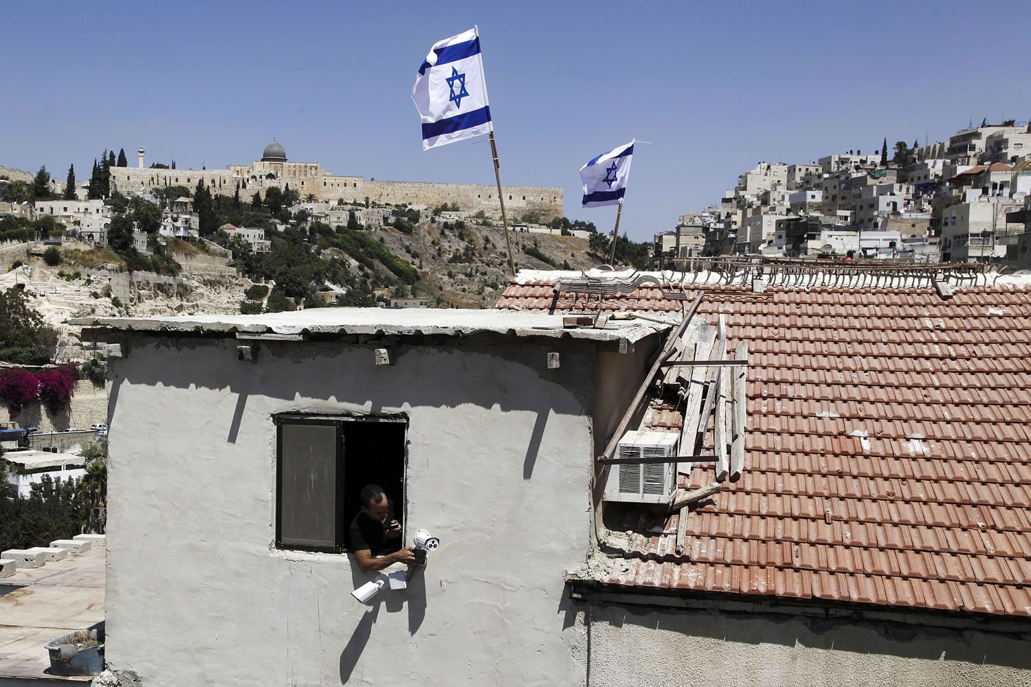 A man leans out a window of a house Thursday in Silwan neighborhood of east Jerusalem with Israeli flags flying above.