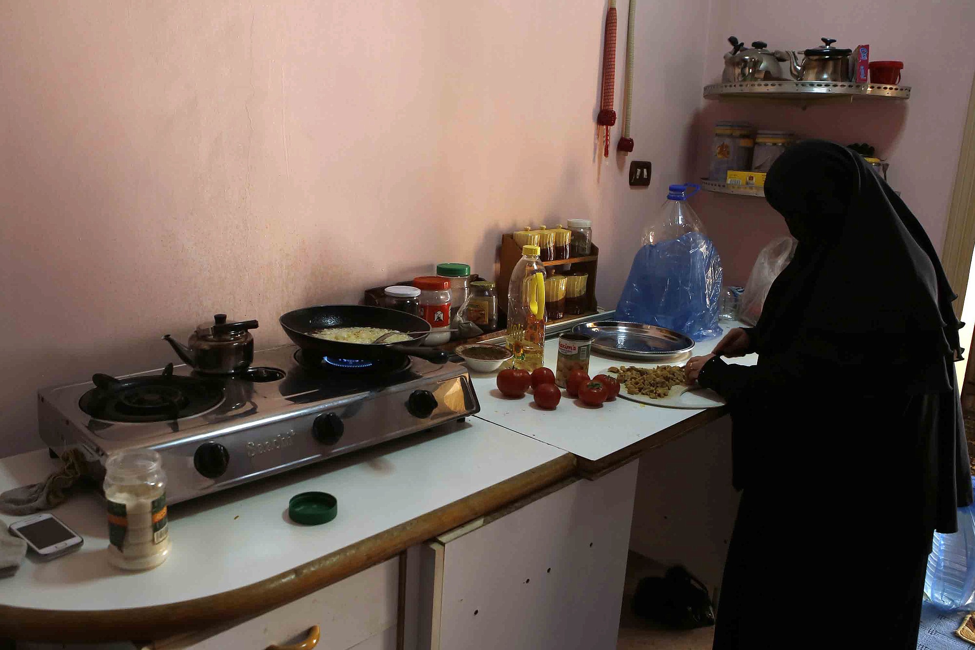 Syrian refugee Rabaa Izzedine, 46, prepares a lunch of fried tomatoes and onions for her husband Issam, 49, in their crowded apartment in Amman, Jordan.