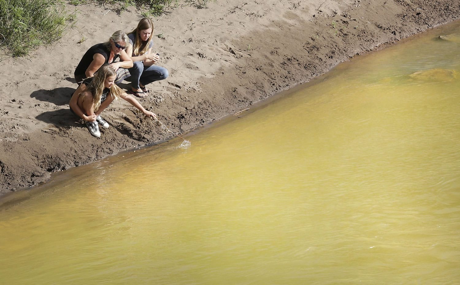 Kim Cofman and her daughters Acacia, 12, left, and Cayenne, 14, try to stir up sludge from the Gold King Mine that covers the bottom the Animas River on Saturday in Durango, Colo., near the 32nd Street Bridge but find the only way to disturb it is to dig into the yellow muck.