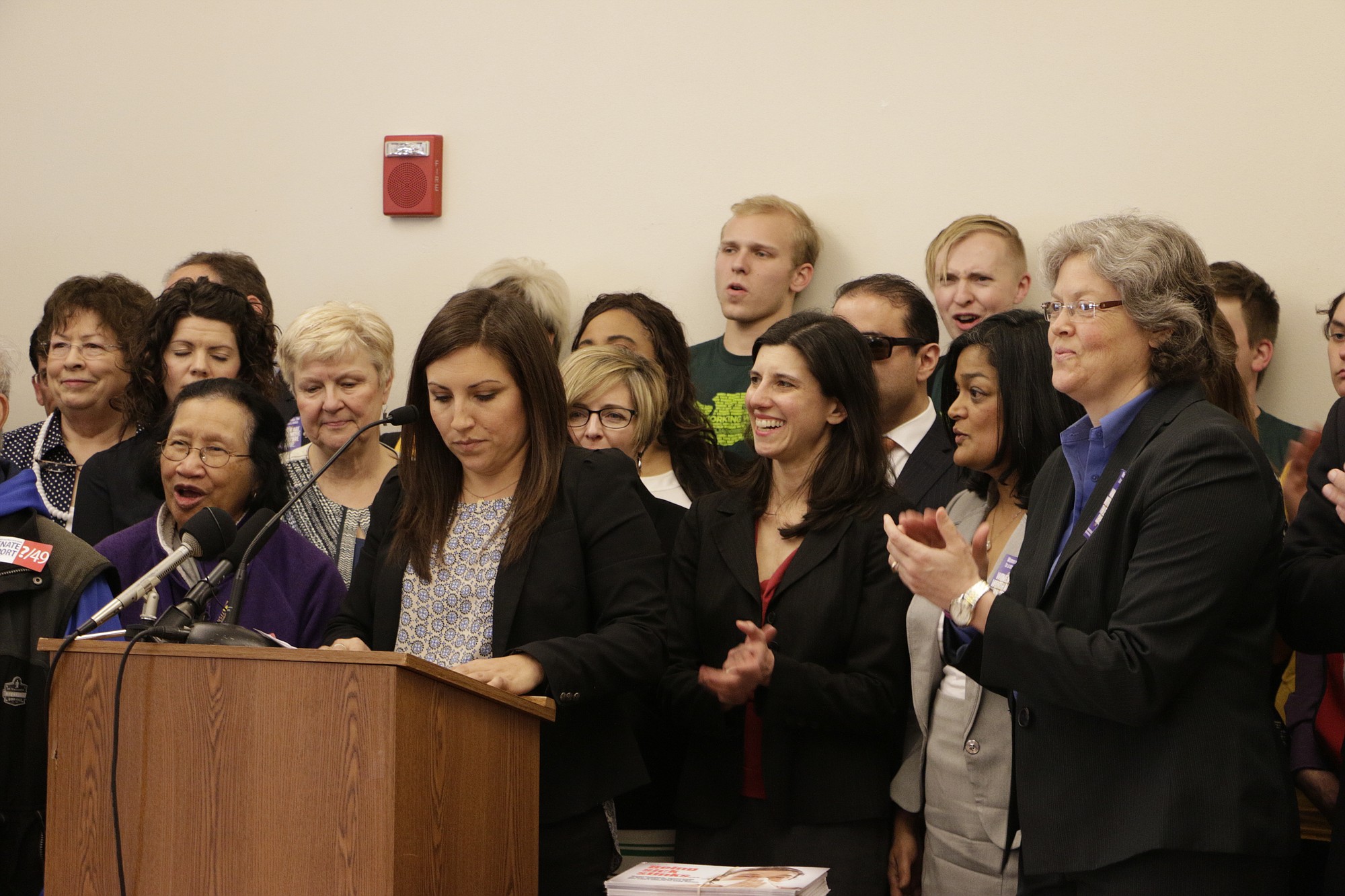 Teresa Mosqueda of the Washington State Labor Council, at podium, is joined by lawmakers and other supporters at a news conference in Olympia on Monday before a hearing on a bill to raise the state's minimum wage to $12 an hour over the next four years.