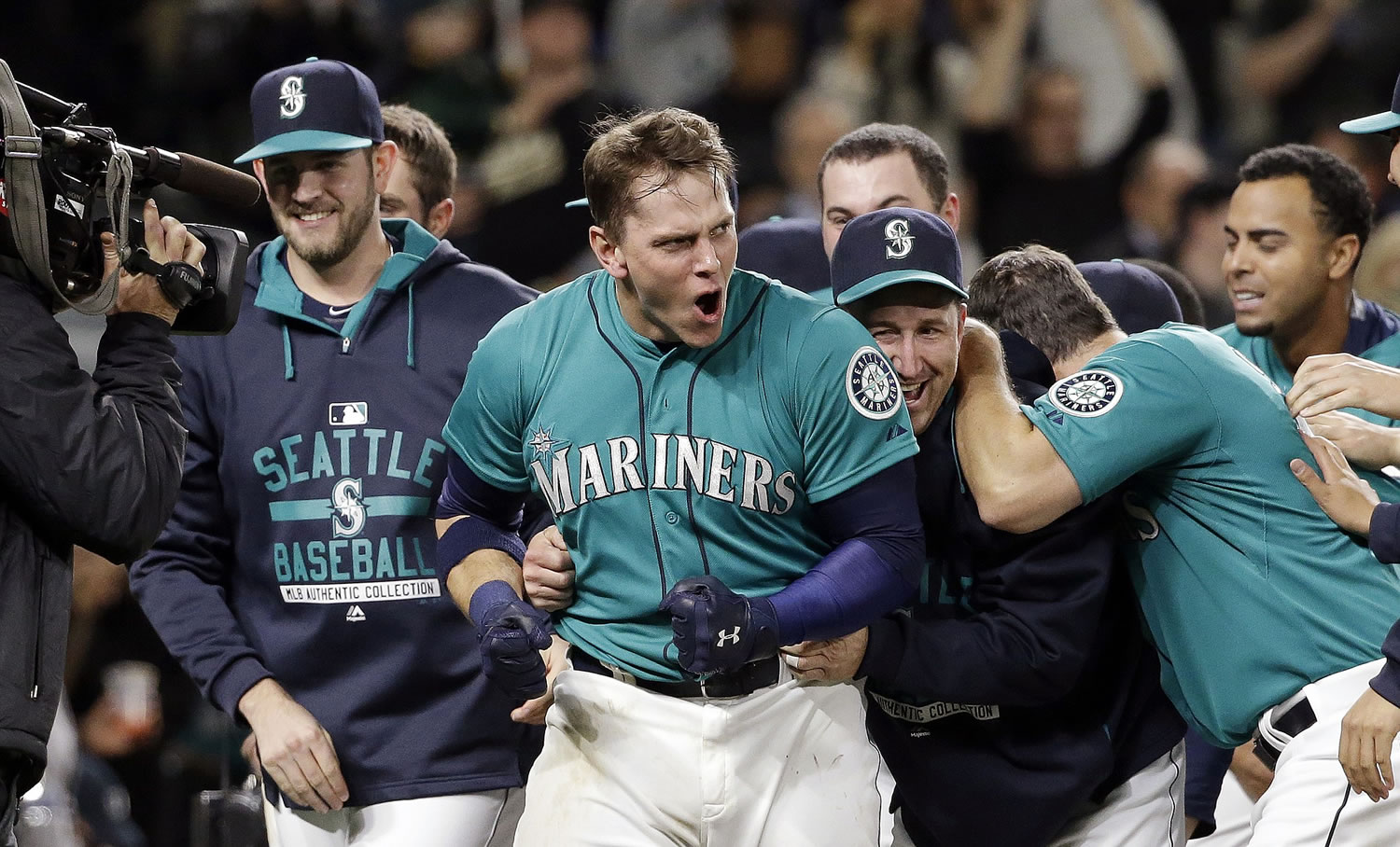 Seattle Mariners' Logan Morrison, center, emerges from a crowd of teammates who crowded around him at home after his walk-off home run against the Oakland Athletics in the 11th inning Friday, May 8, 2015, in Seattle. The Mariners won 4-3.