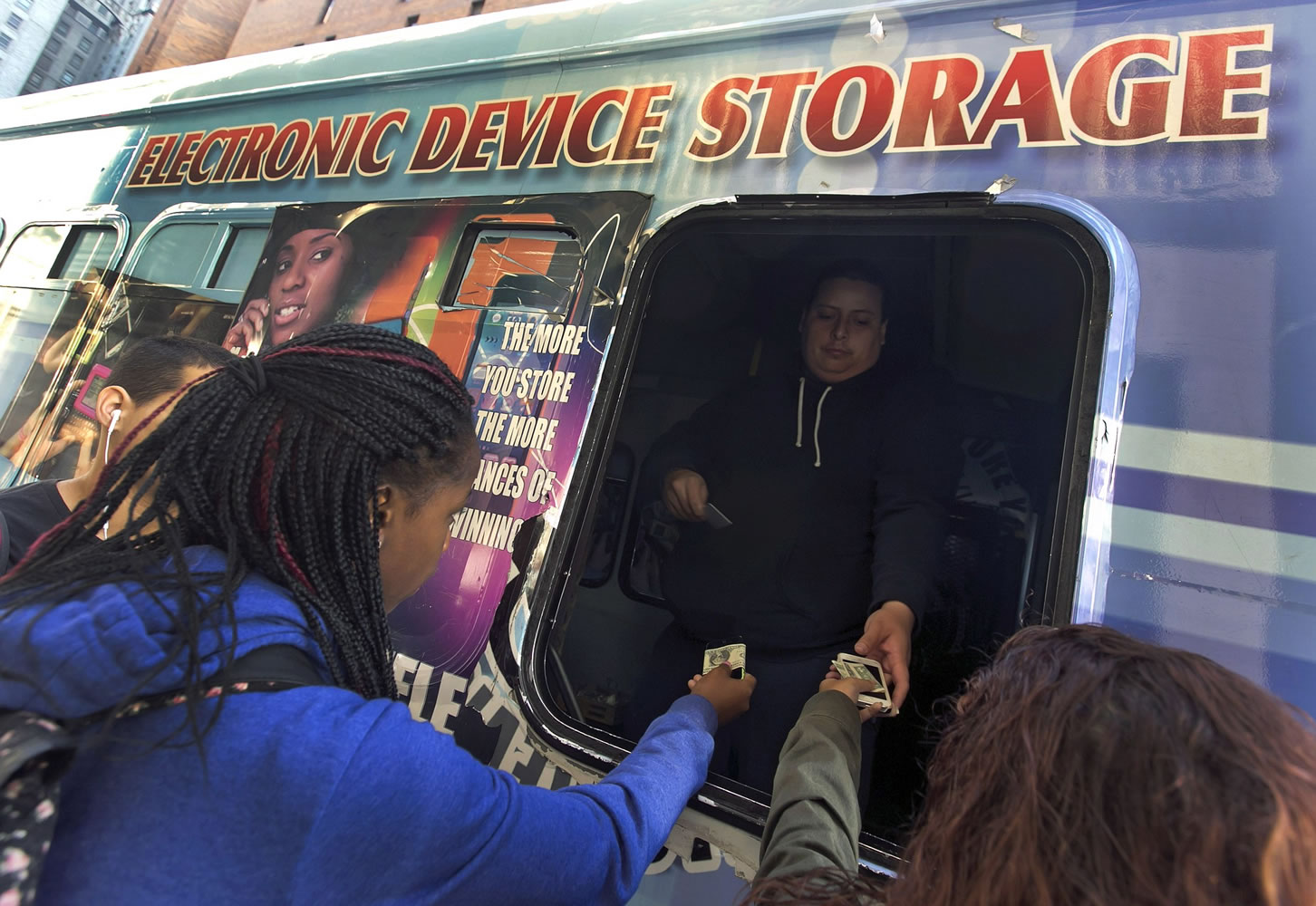 Students from the adjacent Norman Thomas High School building, pay a dollar to driver Rommel Perez to check their electronic devices at a van, before school Thursday.