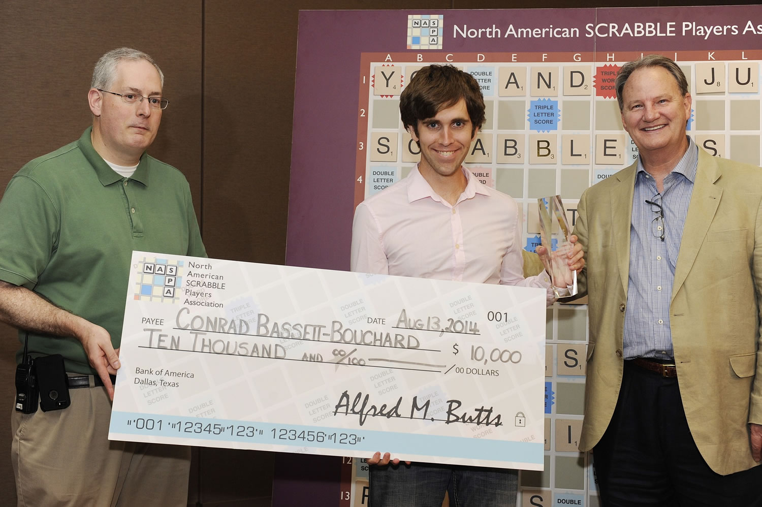 Dallas Johnson, from left, tour director of the North American Scrabble Players Association, holds a check for Conrad Bassett-Bouchard, of Portland, as Chris Cree, co-president of NASPA, stands alongside the champion during the awards ceremony of the National Scrabble Championship, Wednesday, Aug.