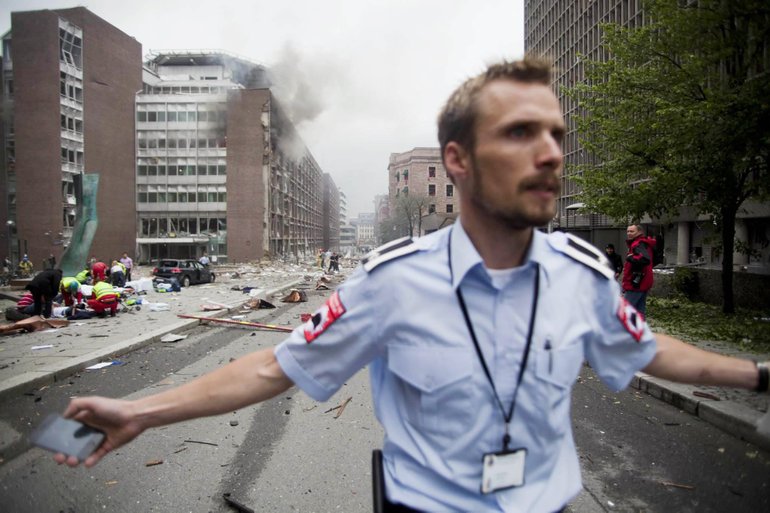 An official attempts to clear away spectators from buildings in the centre of Oslo, Friday July 22, 2010, following an explosion that tore open several buildings including the prime minister's office, shattering windows and covering the street with documents.(AP Photo/Fartein Rudjord)