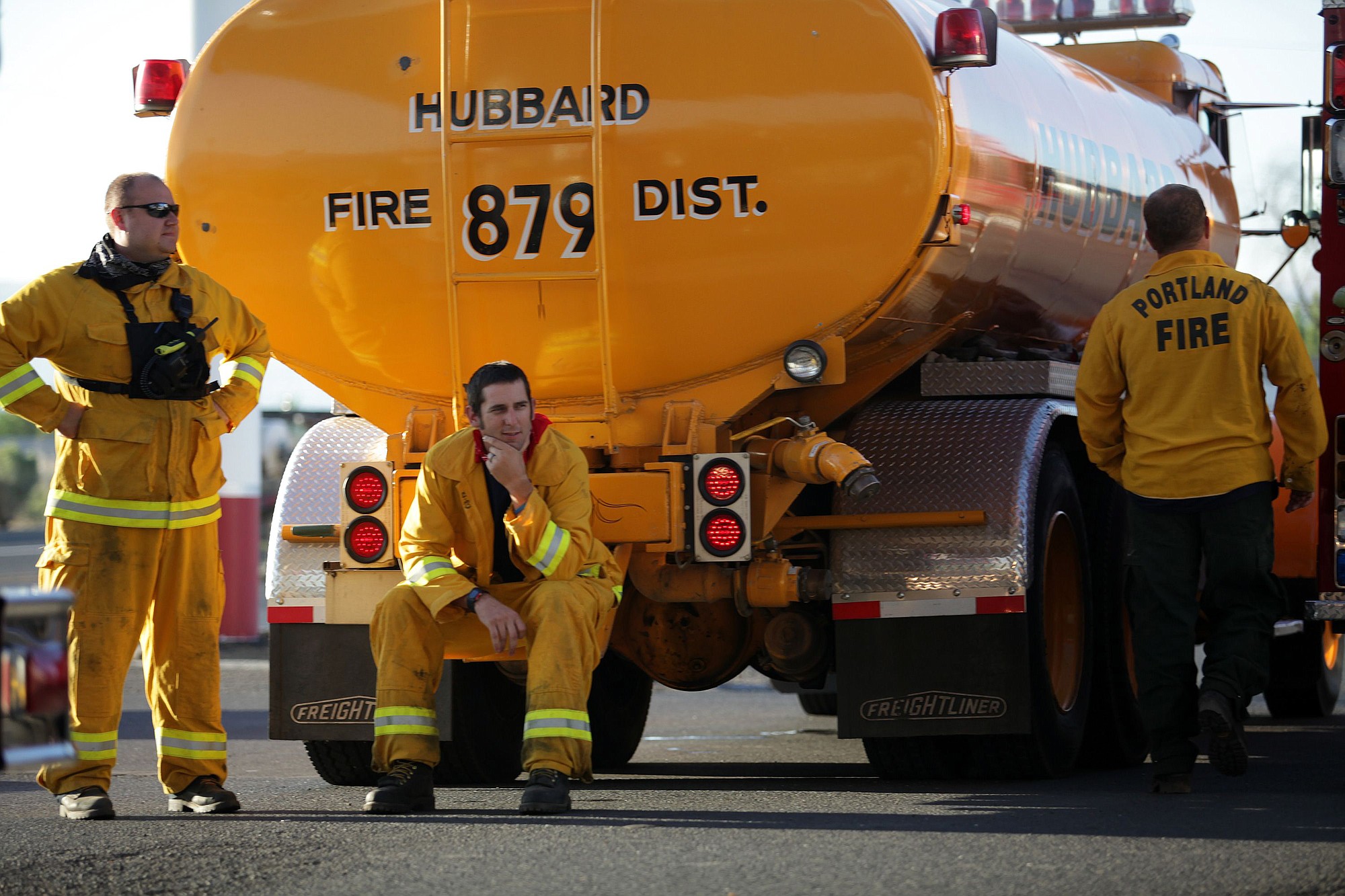A firefighter rests on the back bumper of a Hubbard Fire Department water truck while waiting to refuel after a night on the fire lines.