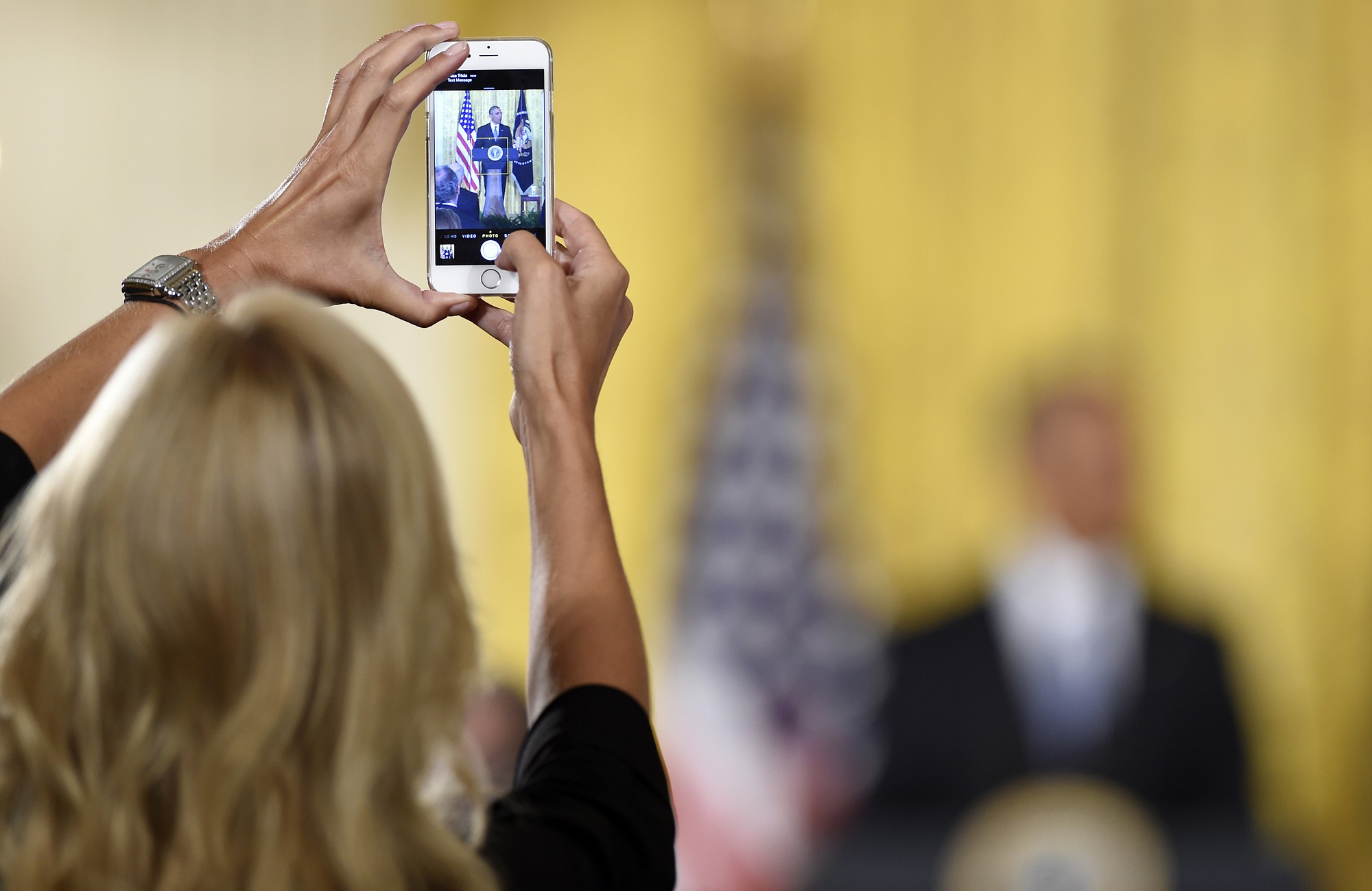 A woman takes a photo of President Barack Obama as he speaks at the 2015 White House Conference on Aging on Monday in the East Room of the White House in Washington.