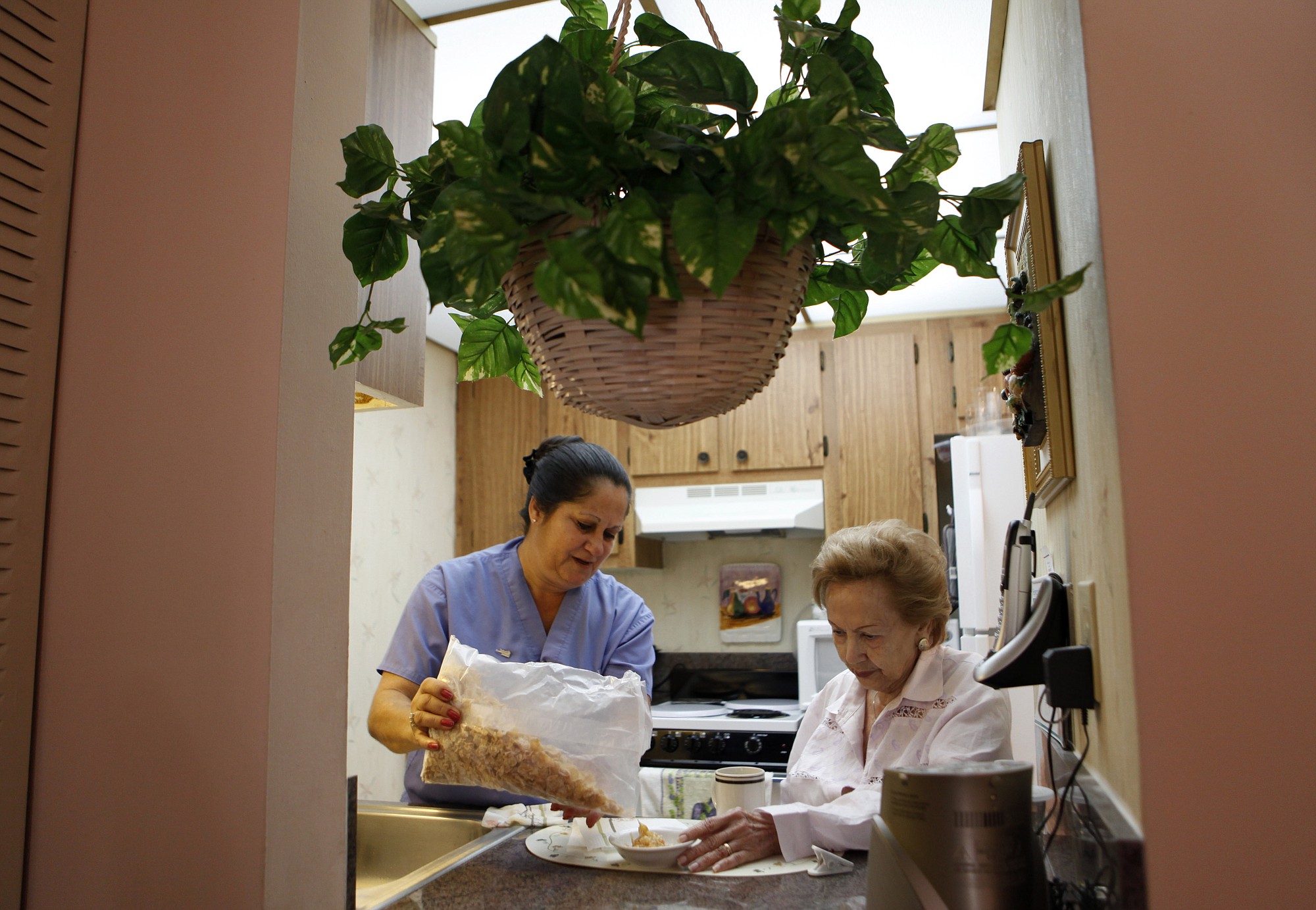 FILE - In this Sept. 3, 2010 file photo, United Home Care Services home health aide Maria Fernandez, left, pours cereal for Herminia Vega, 83, right, as she performs household chores for Vega and her husband, in Miami. On average, nearly 70 percent of people who turn 65 years-old will eventually need some form of long-term care, according to the U.S.
