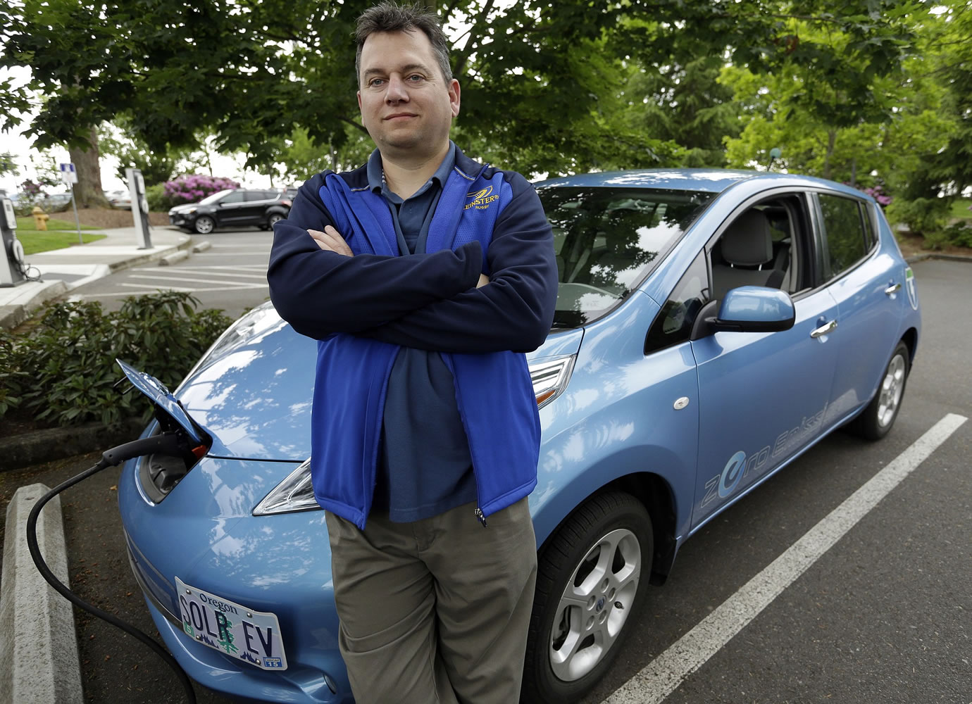 Patrick Conner, who has been driving an electric car since 2007, poses with his Nissan Leaf at a charging station at the public library in Hillsboro, Ore., Tuesday, May 19, 2015.    Fuel-efficient, hybrid and electric cars are a boon for the environment, but their growing popularity means shrinking fuel tax revenues for state coffers and less money to pay for road and bridge projects. Oregon is about to embark on a first-in-the-nation program that aims to address this shortfall by testing the feasibility of taxing motorists not for the fuel they use, but for the miles they drive.