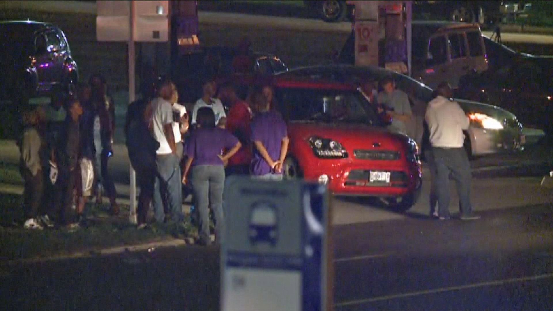 A crowd gathers near the scene where a police officer was shot in the arm Saturday night in Ferguson, Mo. The officer was shot in the arm and is expected to survive, St.