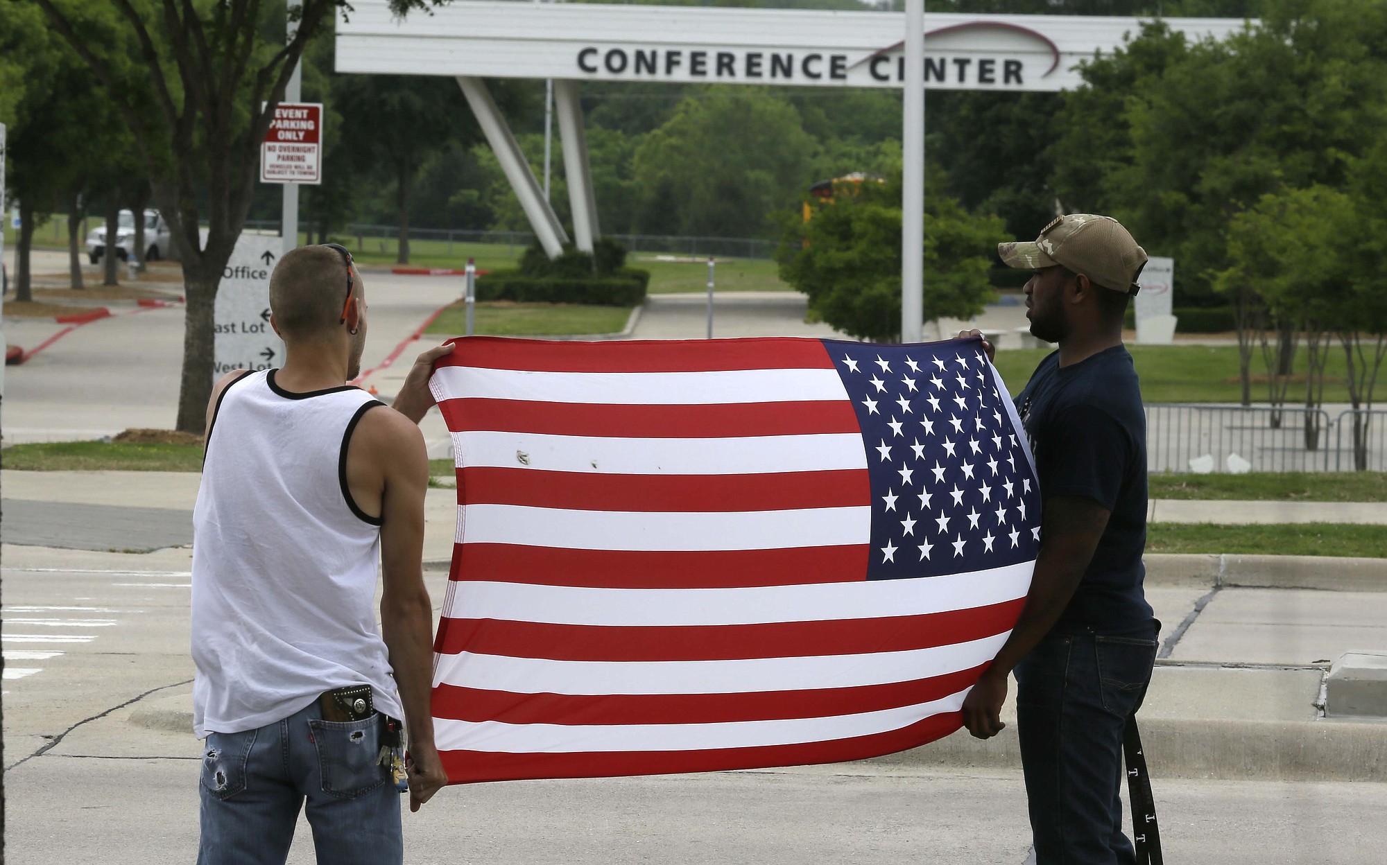 Joseph Offutt, right, and Conner McCasland hold a U.S. flag across the street from the Curtis Culwell Center, on Tuesday in Garland, Texas. A man whose social media presence was being scrutinized by federal authorities was one of two suspects in the Sunday shooting at this location that hosted a cartoon contest featuring images of the Muslim Prophet Muhammad.