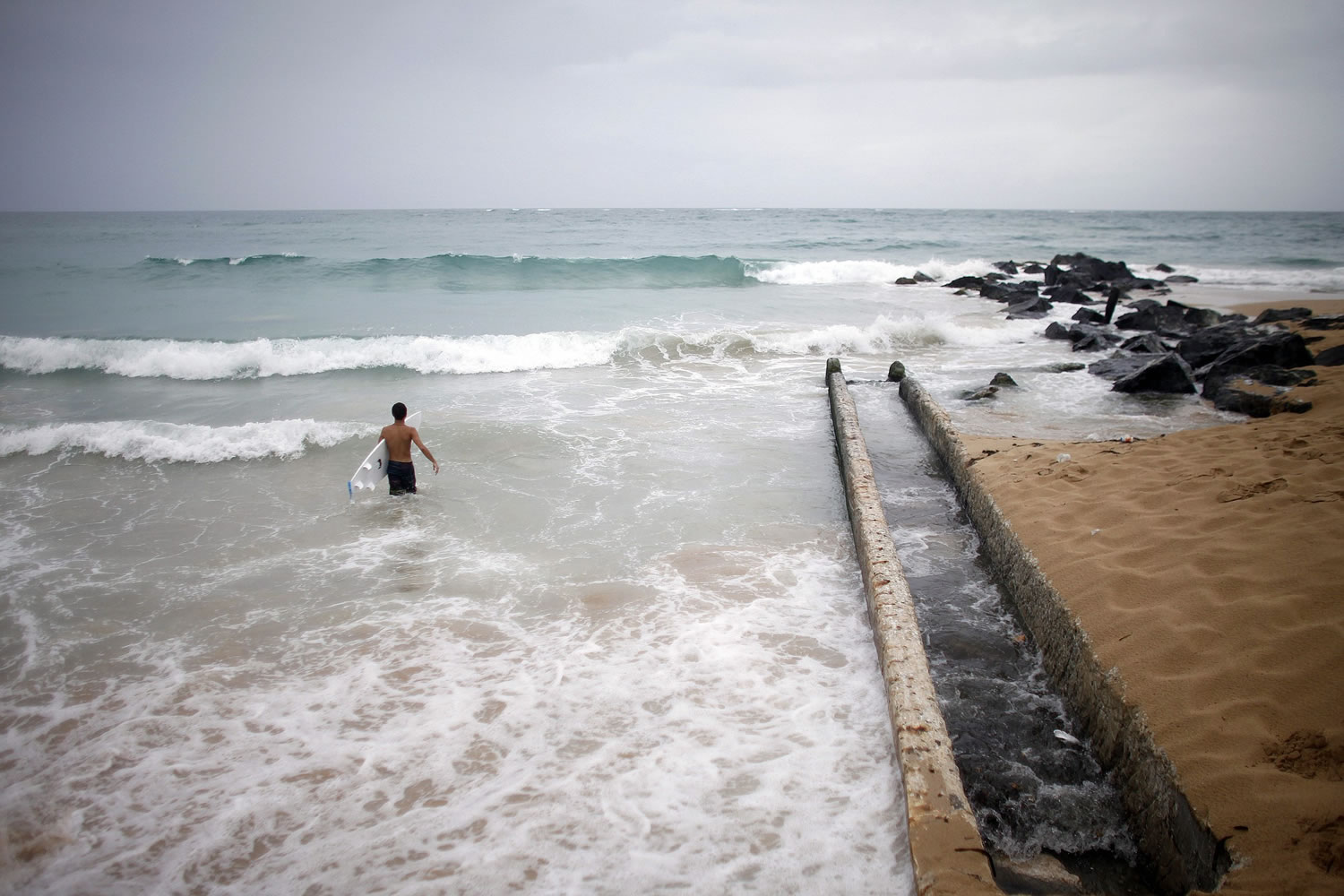 A surfer enters the water Saturday to take advantage of the high waves in San Juan, Puerto Rico.