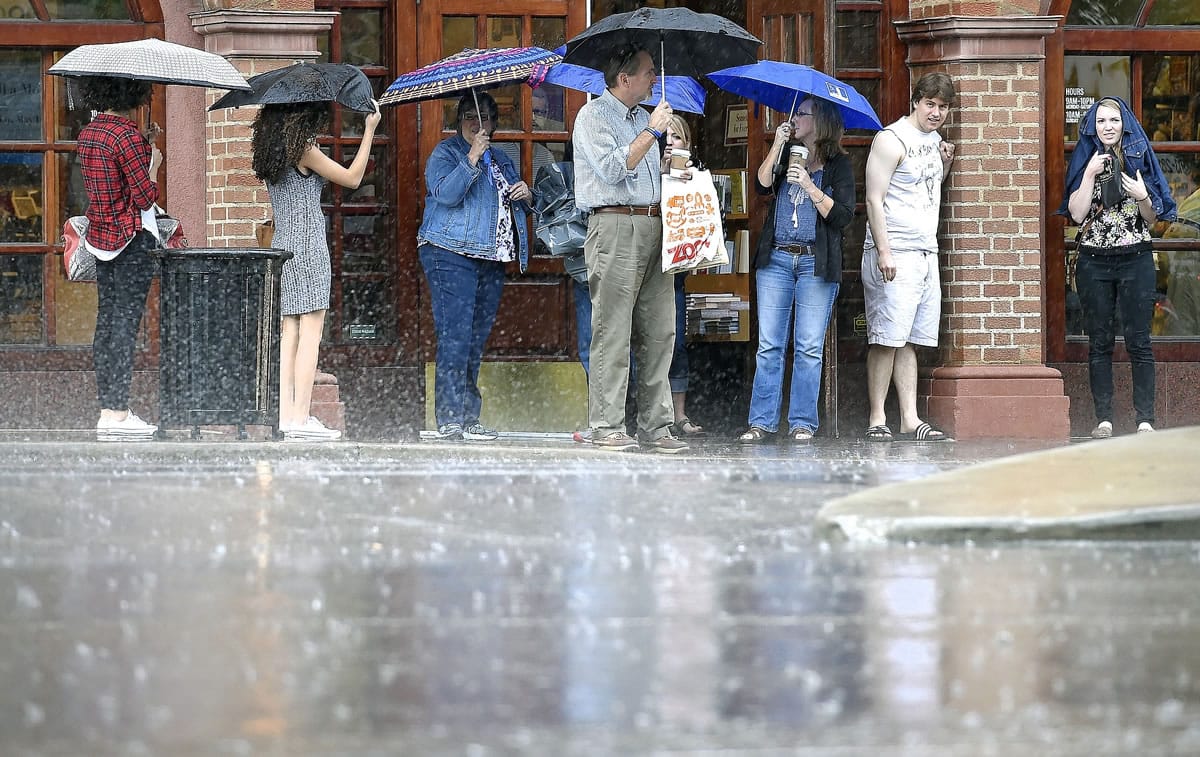 An afternoon rainstorm forces shoppers on the Country Club Plaza to pull out their umbrellas or do without as they wait outside the Barnes