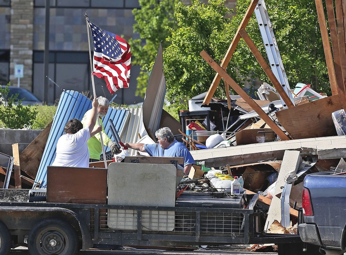 Jim Bresee, center, smiles as his daughter, Sandra Silvy, left, raises a flag in what is left of the Bresee's storage unit following Wednesday's storm  in Oklahoma City, on Thursday. His wife Carol Bresee is at right. The three are attempting to salvage what they can from the unit, but much is damaged due to rain. Gov.