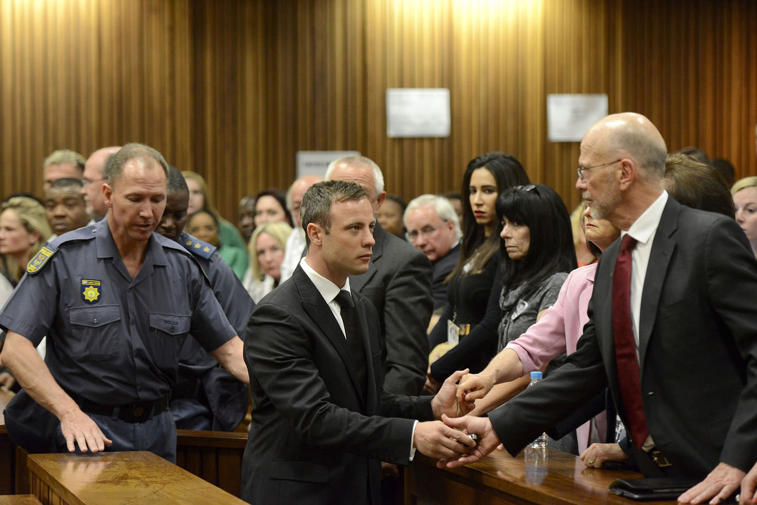 Oscar Pistorius, left, greets his uncle Arnold Pistorius, right, and other family members as he is led down to the cells of the court in Pretoria, South Africa, today.