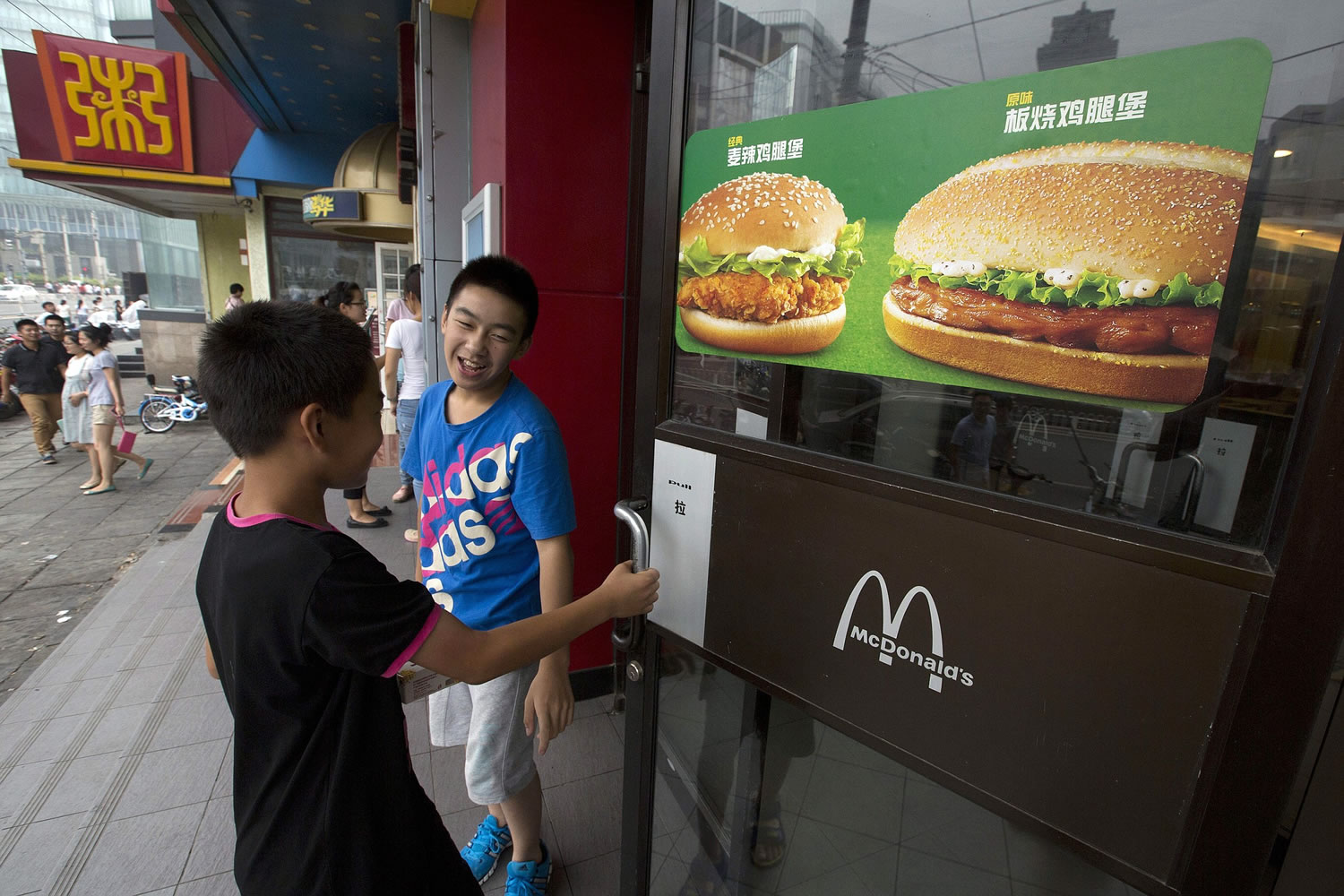 Boys open the door to a McDonald's restaurant July 31 in Beijing. Long a symbol of American economic might, the rising dollar is denting the earnings of U.S.