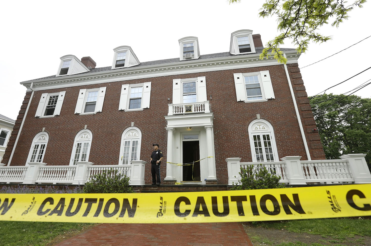 A Tufts University law enforcement official stands behind caution tape Sunday outside the Delta Tau Delta fraternity house, in Somerville, Mass.
