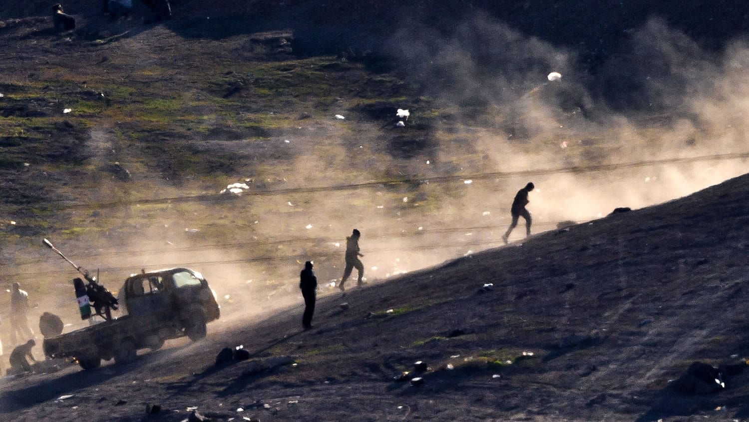 Fighters run on a hillside Tuesday after shooting a heavy machine gun toward the positions of the Islamic State group on the outskirts of Kobani, as seen from the Kara Ali village on the Turkish side of the Turkey-Syria border.