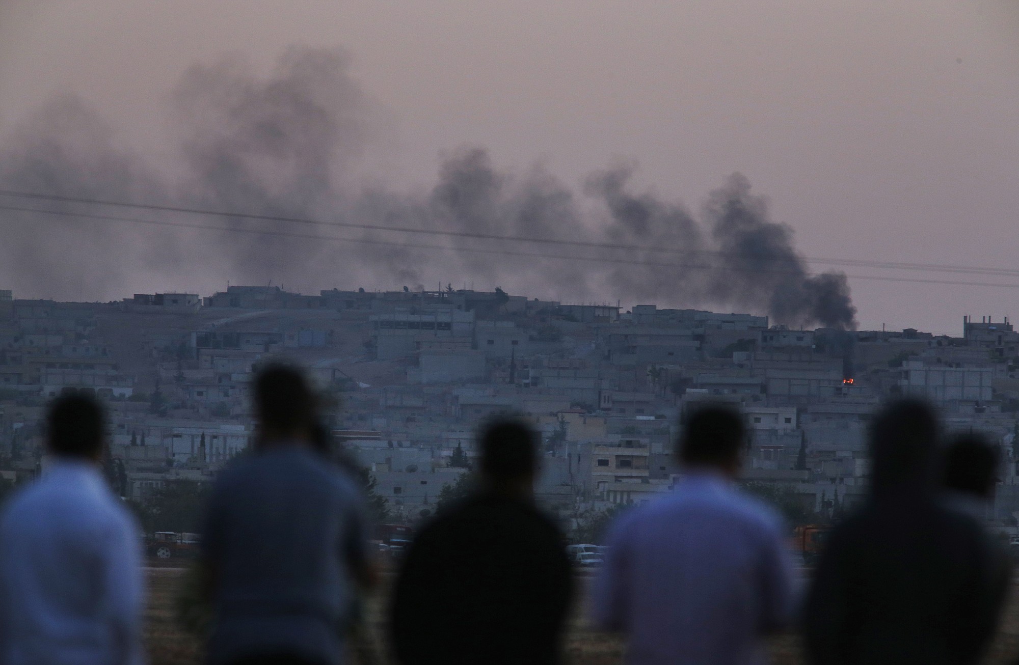 Turkish Kurds standing in the outskirts of Suruc, on the Turkey-Syria border, watch as smoke rises from a fire following an airstrike in Kobani, Syria, where the fighting between militants of the Islamic State group and Kurdish forces intensified on Tuesday.