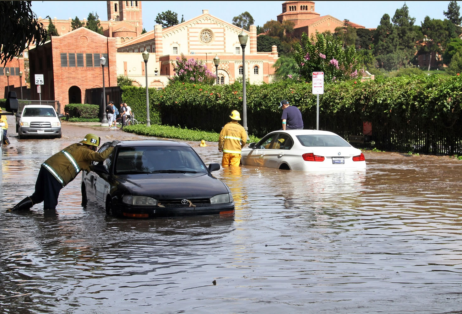 Los Angeles firefighters help drivers whose cars became stranded on Sunset Boulevard after a 30-inch water main broke and sent water flooding down Sunset and onto the UCLA campus, background, in the Westwood section of Los Angeles on Tuesday.