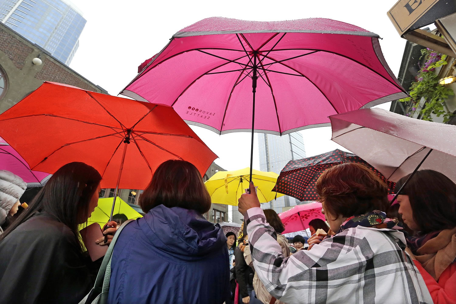 A group of tourists from Korea huddle under umbrellas at the Pike Place Market on Wednesday morning in Seattle.