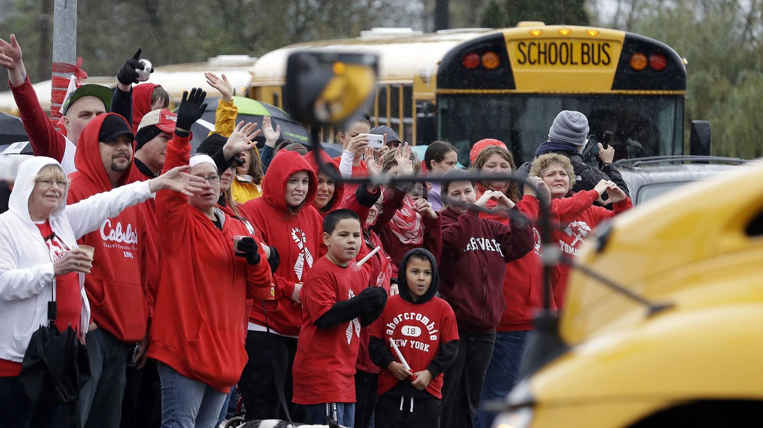 People dressed in the school colors of red and white cheer and wave as school buses carrying students on their return to Marysville-Pilchuck High School drive past Monday, Nov. 3, 2014, in Marysville, Wash. After the shock from the Oct. 24 shooting there that left four students dead, including the shooter, and two students still in a Seattle hospital, administrators and teachers hope to transition to a new routine. The day was scheduled to begin with a morning assembly. Lunch is in the gym because the cafeteria where the shooting took place remains closed.