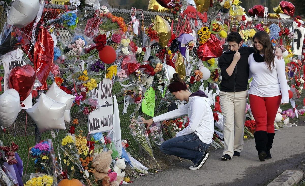 Dana Pattie, left, kneels at a block-long fence at Marysville-Pilchuck High School memorializing a shooting there last week as a couple walks past Wednesday in Marysville.