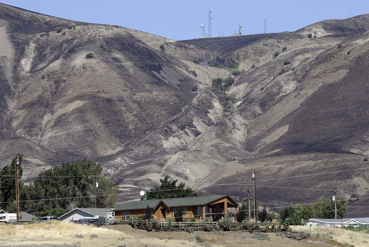Fire-blackened hills above a residence in Roosevelt, Wash., shows how close an early morning wildfire came to the town, Wednesday, Aug. 5, 2015.   Residents, who evacuated overnight, have returned to their homes and the fire is headed away for the town.