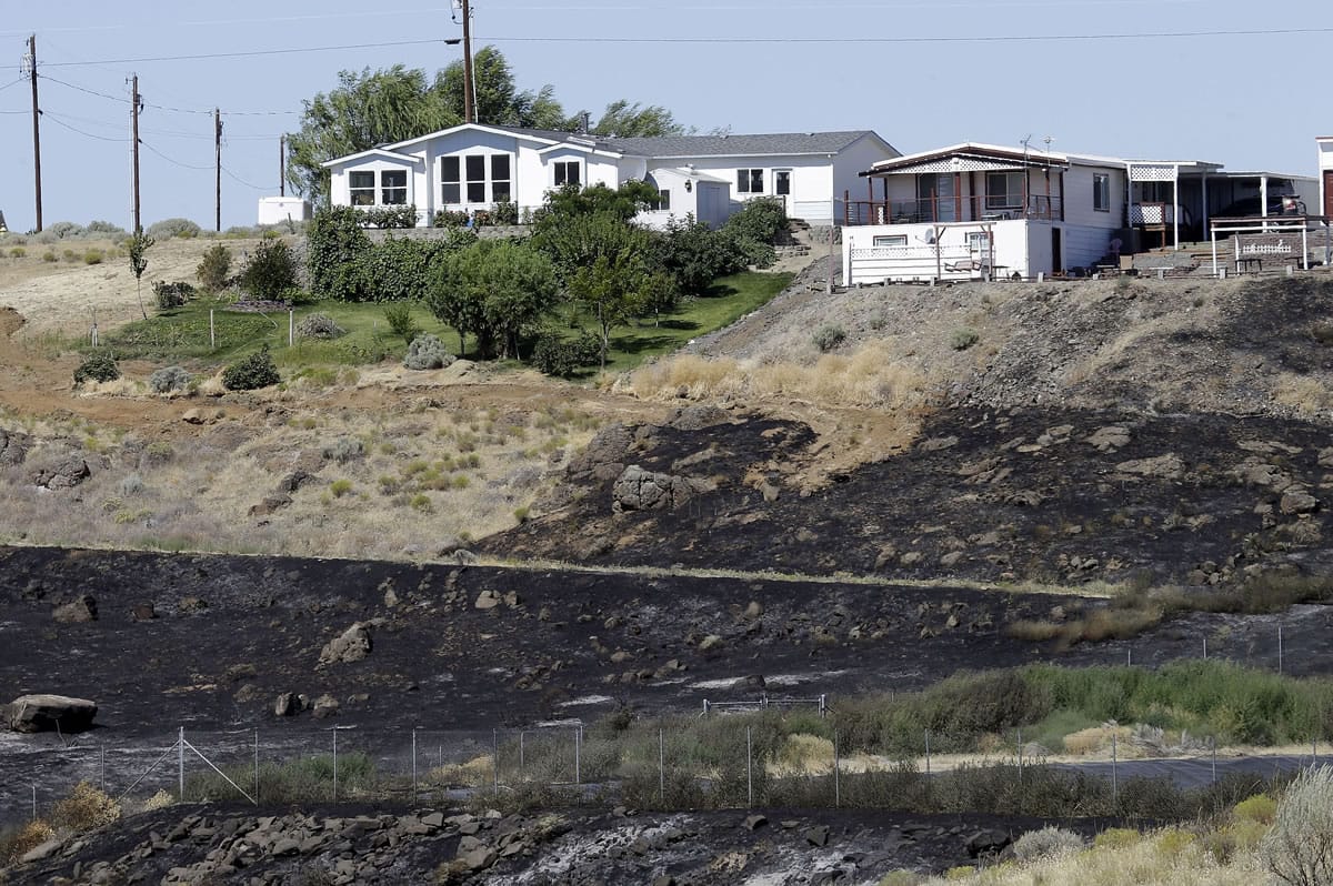 Fire-blackened ground below residences in Roosevelt, Wash., shows how close an early morning wildfire came to the town Wednesday, Aug. 5, 2015.  Residents, who evacuated overnight, have returned to their homes and the fire is headed away for the town.