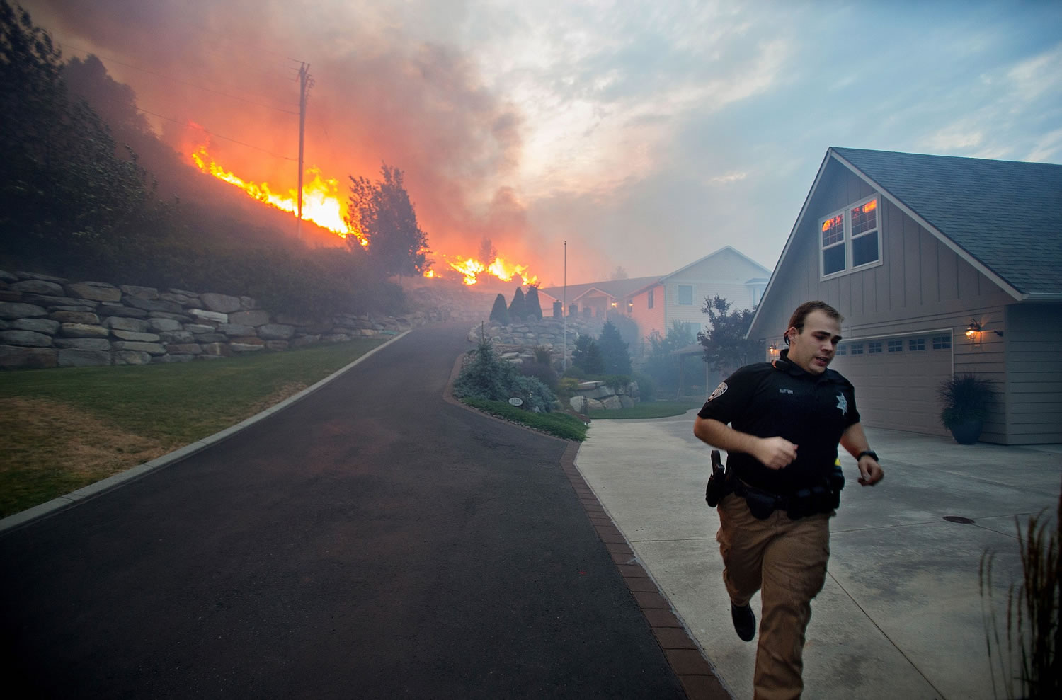 A Chelan County Sheriff's deputy races to check that all residents have left their homes Sunday as flames approach houses at Quail Hollow Lane in Wenatchee.