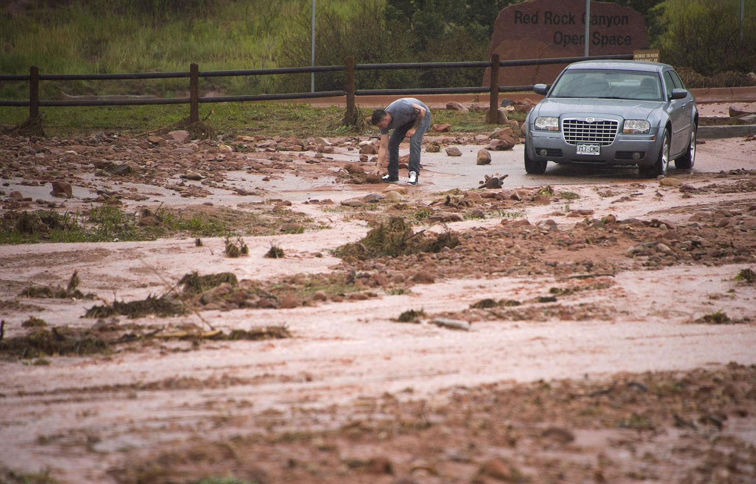 A motorist clears rocks from his path before driving his car down the flooded entrance road to Red Rock Canyon Open Space in Colorado Springs, Colo., on Tuesday morning.