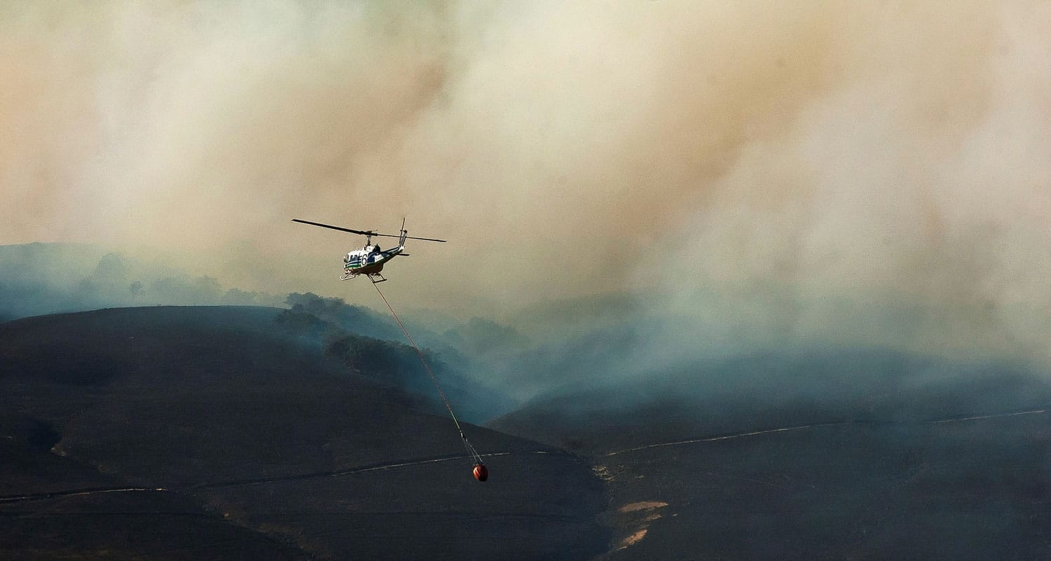 A helicopter drops water into a ravine just west of Chenowith Street as the fight to stop the Rowena Fire west of The Dalles, Ore., on Thursday.