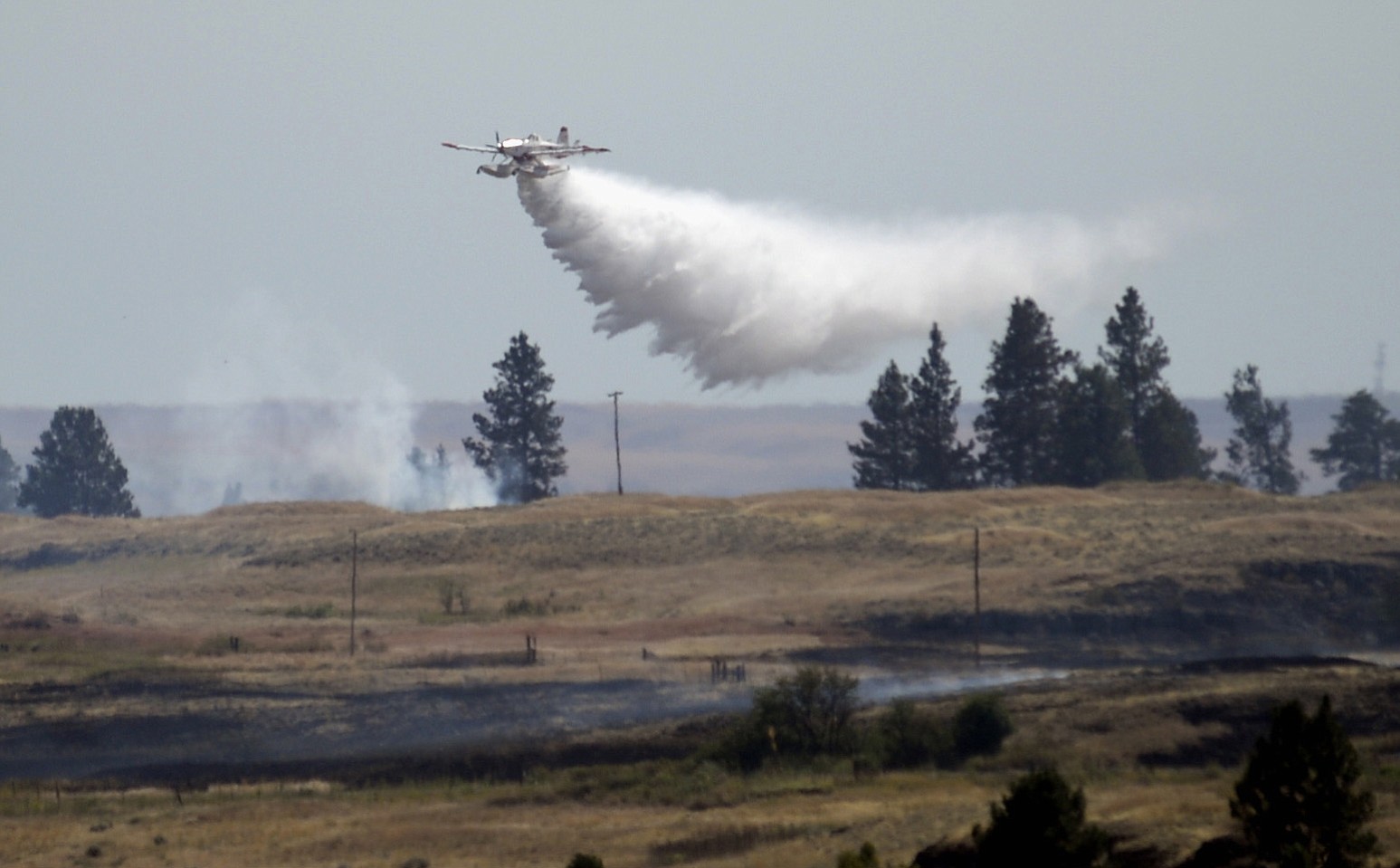 A firefighting plane drops water from Fishtrap Lake on a stubborn fire burning Sunday near the lake in Lincoln County, near Cheney.