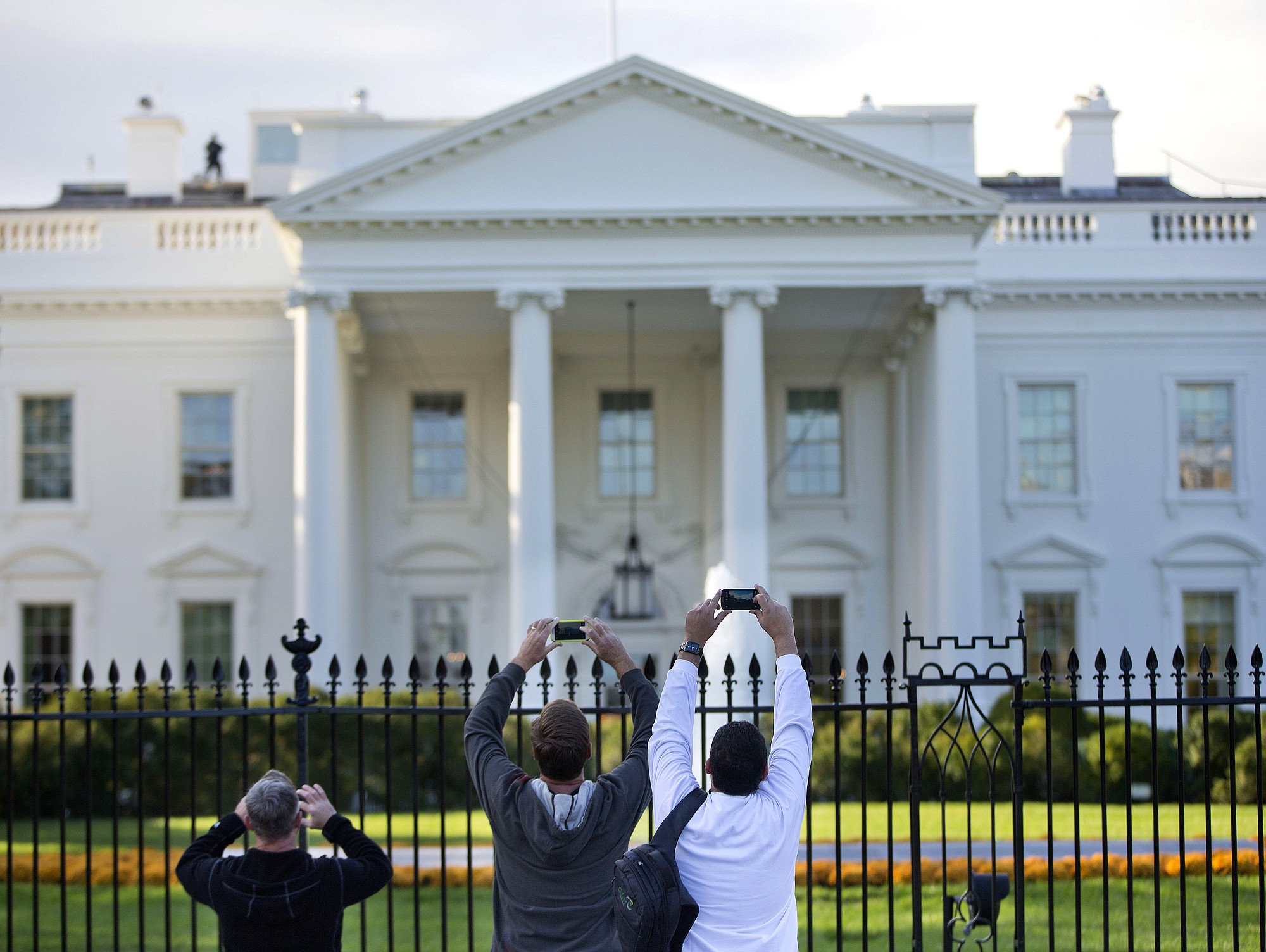 Visitors take photos of the White House on the sidewalk in front of the White House in Washington on Thursday.