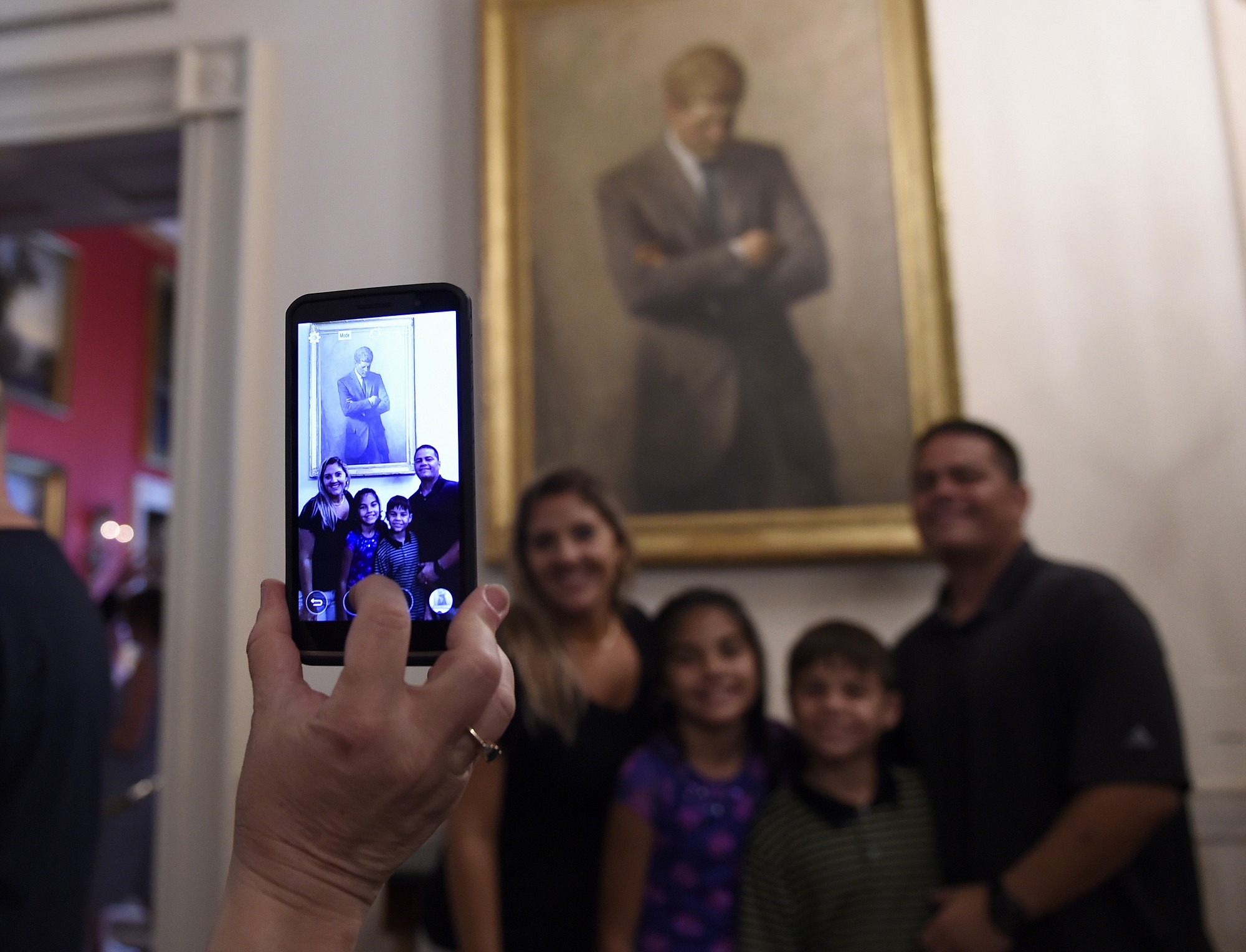 A group has their photo taken in front of a portrait of President John F.