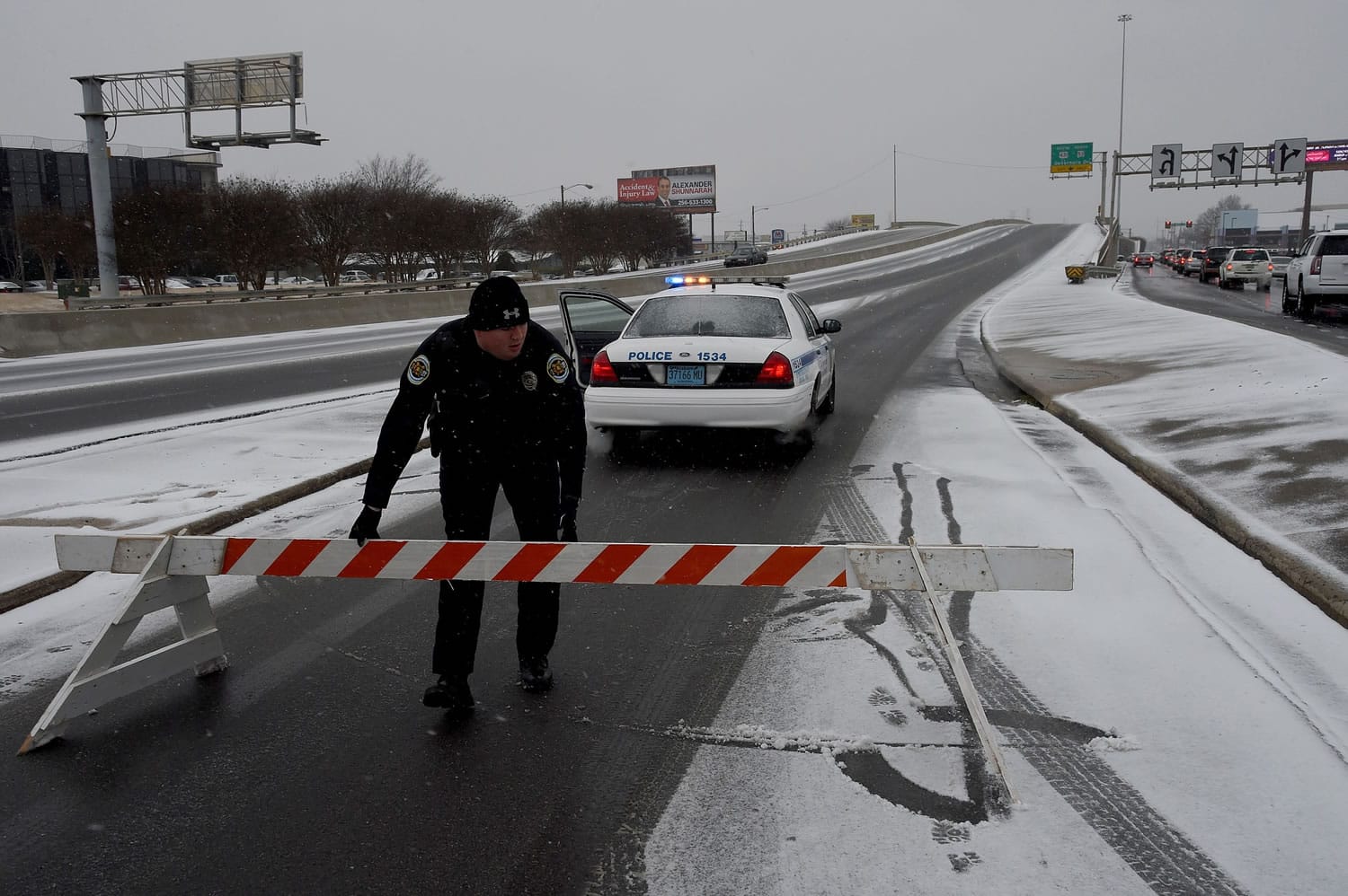 Huntsville Police officer Clark places barricades at the entrance to South Memorial Parkway at Bob Wallace Avenue as snow begins to fall as another winter storm pushes through the Tennessee Valley on Friday in Huntsville, Ala.