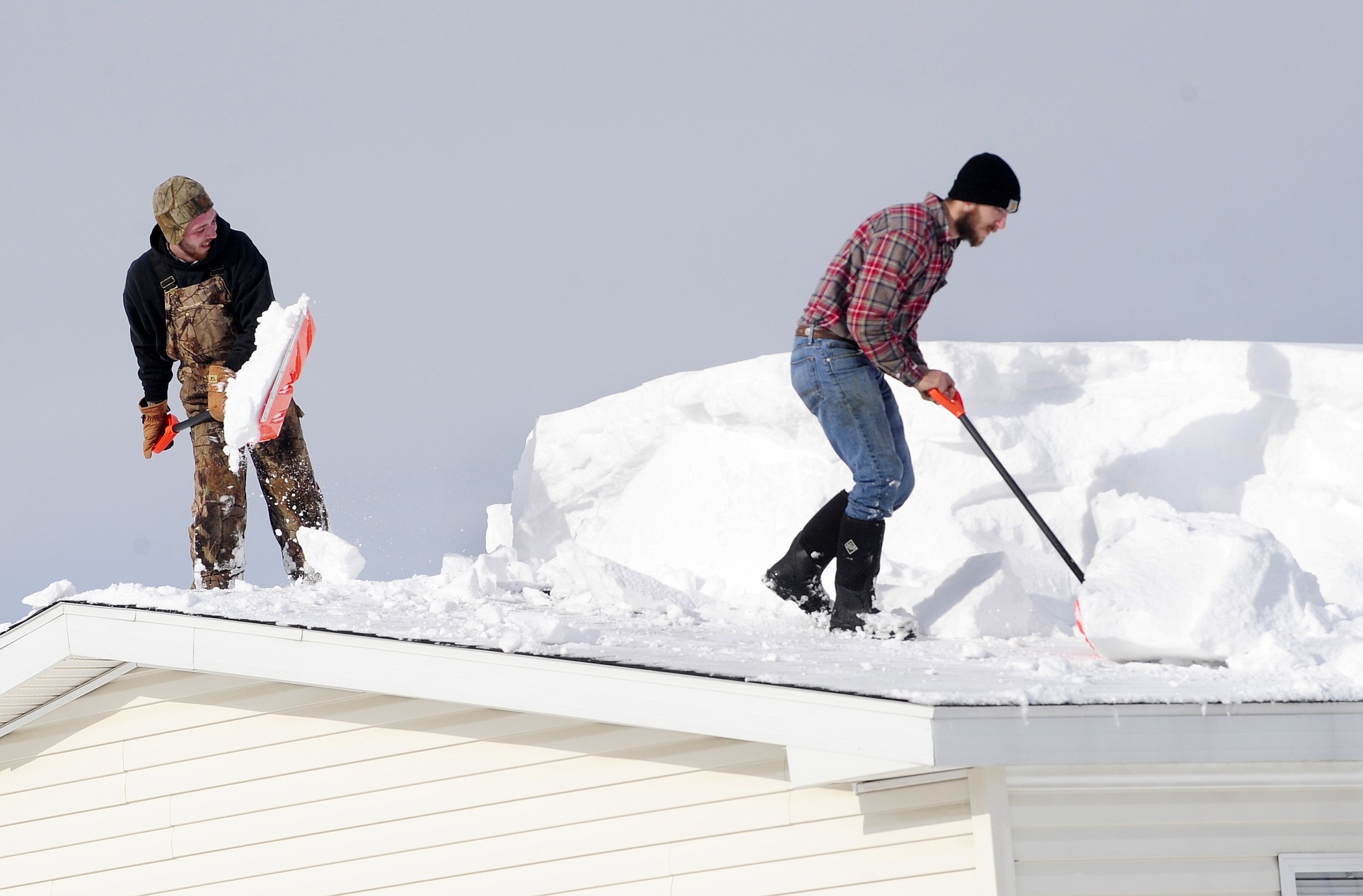 D.J. Schloss, left, and Doug Metz, right shovel off a roof on Abbey Lane in Alden, N.Y., on Thursday.