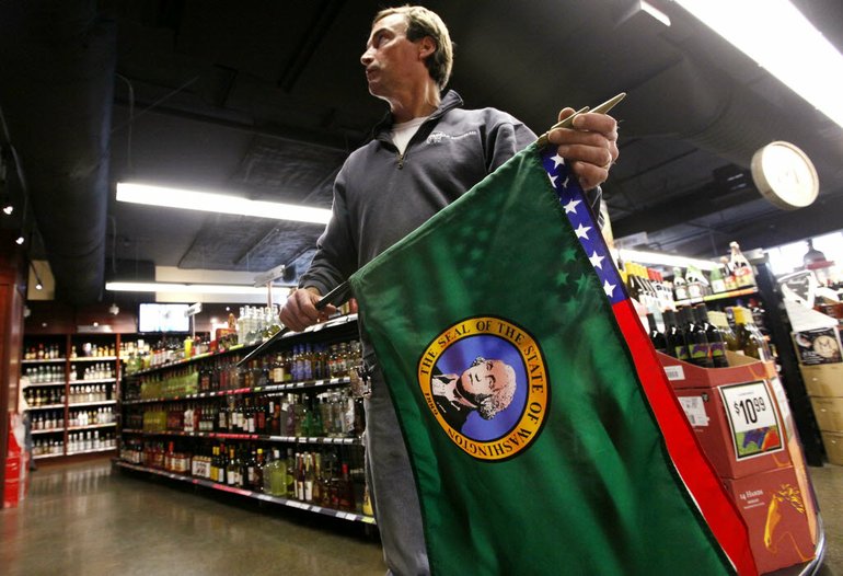 Liquor Control Board carpenter Mark Terhune holds a state and a U.S. flag as he prepares to install them Monday at a new state liquor store in the West Seattle neighborhood of Seattle. Almost half of Washington voters say they support a plan to privatize the state's liquor distribution system, according to a University of Washington poll released Monday. The survey found that about 48 percent of respondents planned to vote yes on Initiative 1183, which would end state-run liquor sales and allow private businesses to sell the product in their stores.