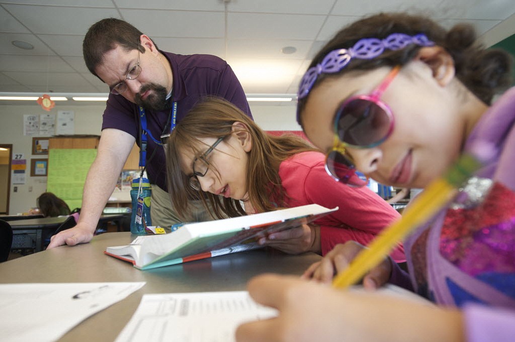 Substitute teacher and Washington State University Vancouver graduate Bryan Moxley helps fifth graders Anastazia McCusker, 11, center, and Monique Williams, 11, at Chief Umtuch Middle School on May 14, 2014.