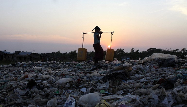 A Myanmar woman walks across a garbage dump Thursday as she carries drinking water in plastic containers in Dalla, about 15 kilometers south of Yangon, Myanmar.