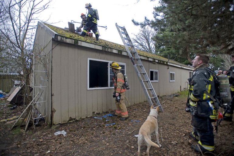 Firefighters ventilate the roof of a home on Tuesday after knocking out a fire inside the structure near the Vancouver Plaza shopping center.
