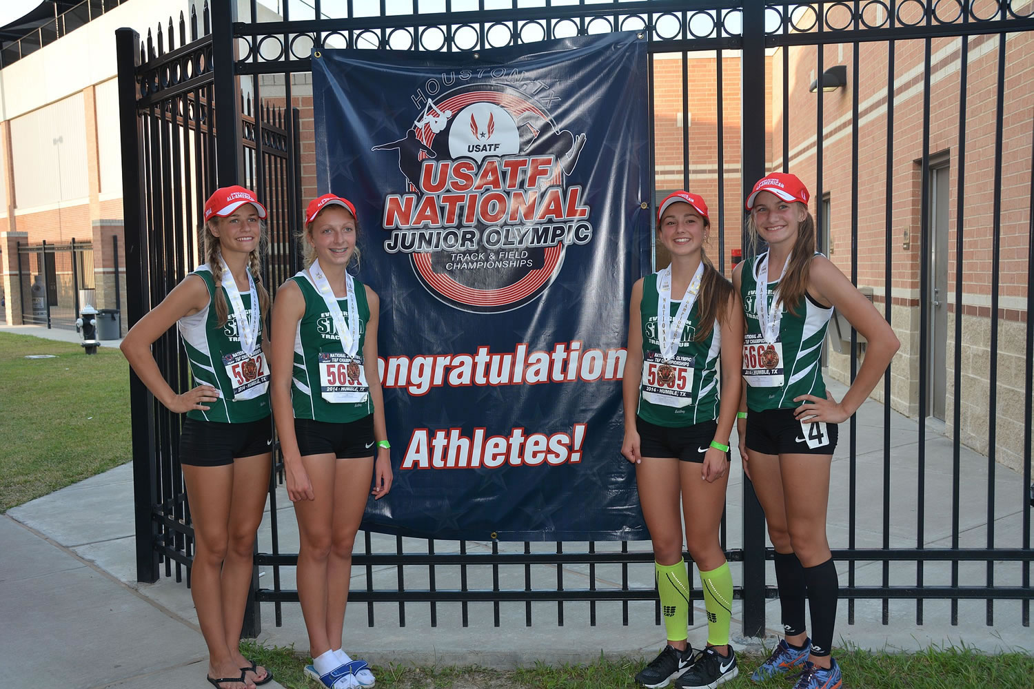 Members of the Evergreen Storm Track Club 4x800 meter relay pose by a banner at the USATF National Junior Olympic Championships on Wednesday in Houston. The team placed third among girls ages 13-14.
