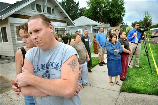 Neighbors line the side walk as emergency crews battle to save six people pulled from a burning home on West 10th Street in Medford, Ore., Monday July 18, 2011. A mother and her four young children who were pulled from the burning house had stab wounds and died, and the father was under police watch.