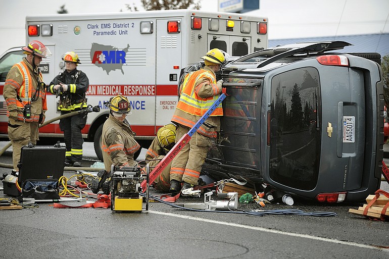 Firefighters with the Vancouver Fire Department work to rescue a woman trapped in an overturned van after an accident involving another vehicle at the intersection of Northeast Fourth Plain Boulevard and Northeast Vancouver Mall Drive.