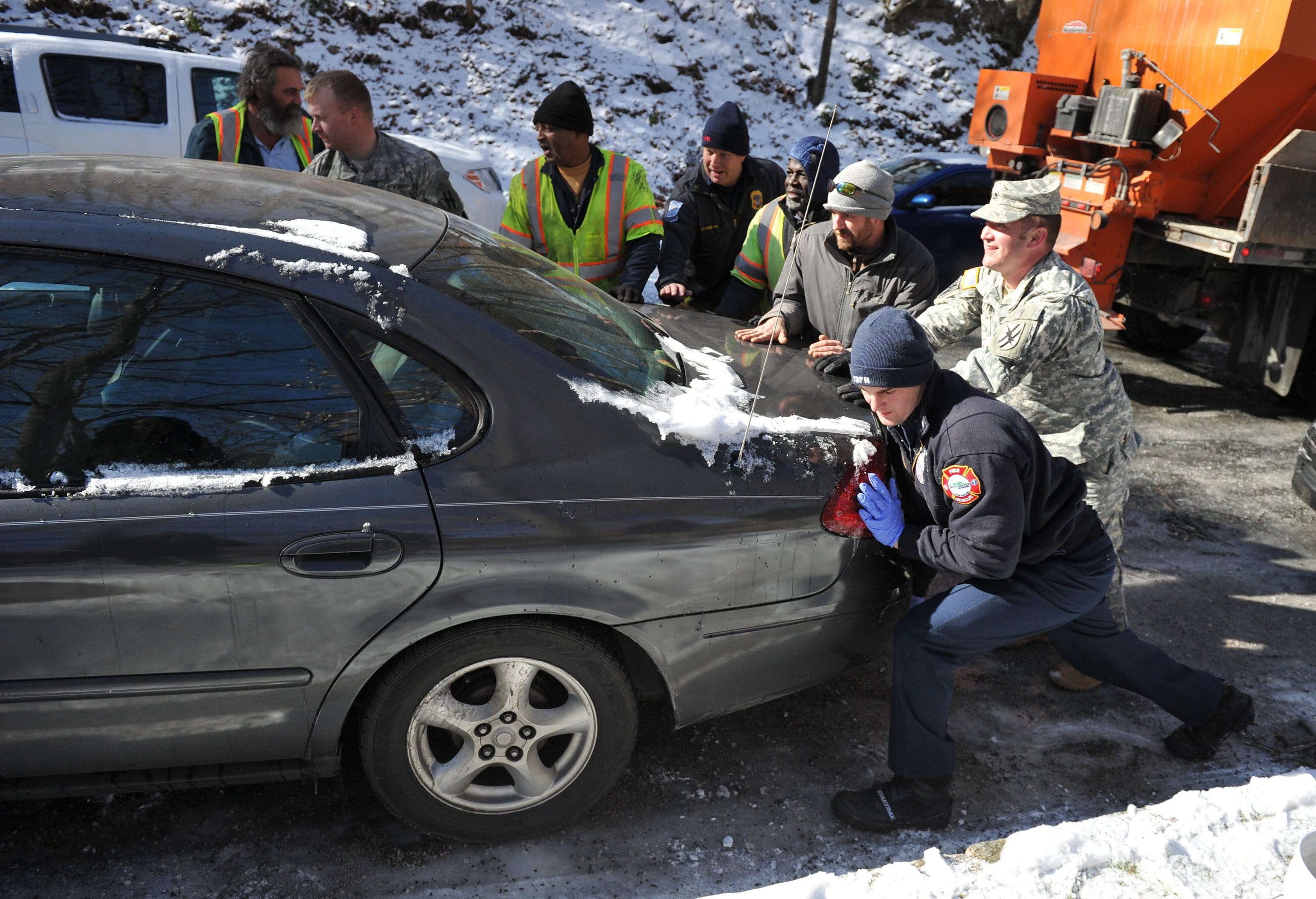 Contractors, volunteers and members of the Georgia National Guard move a car that was blocking the road, preventing a salt truck from treating a hill Thursday in Atlanta.