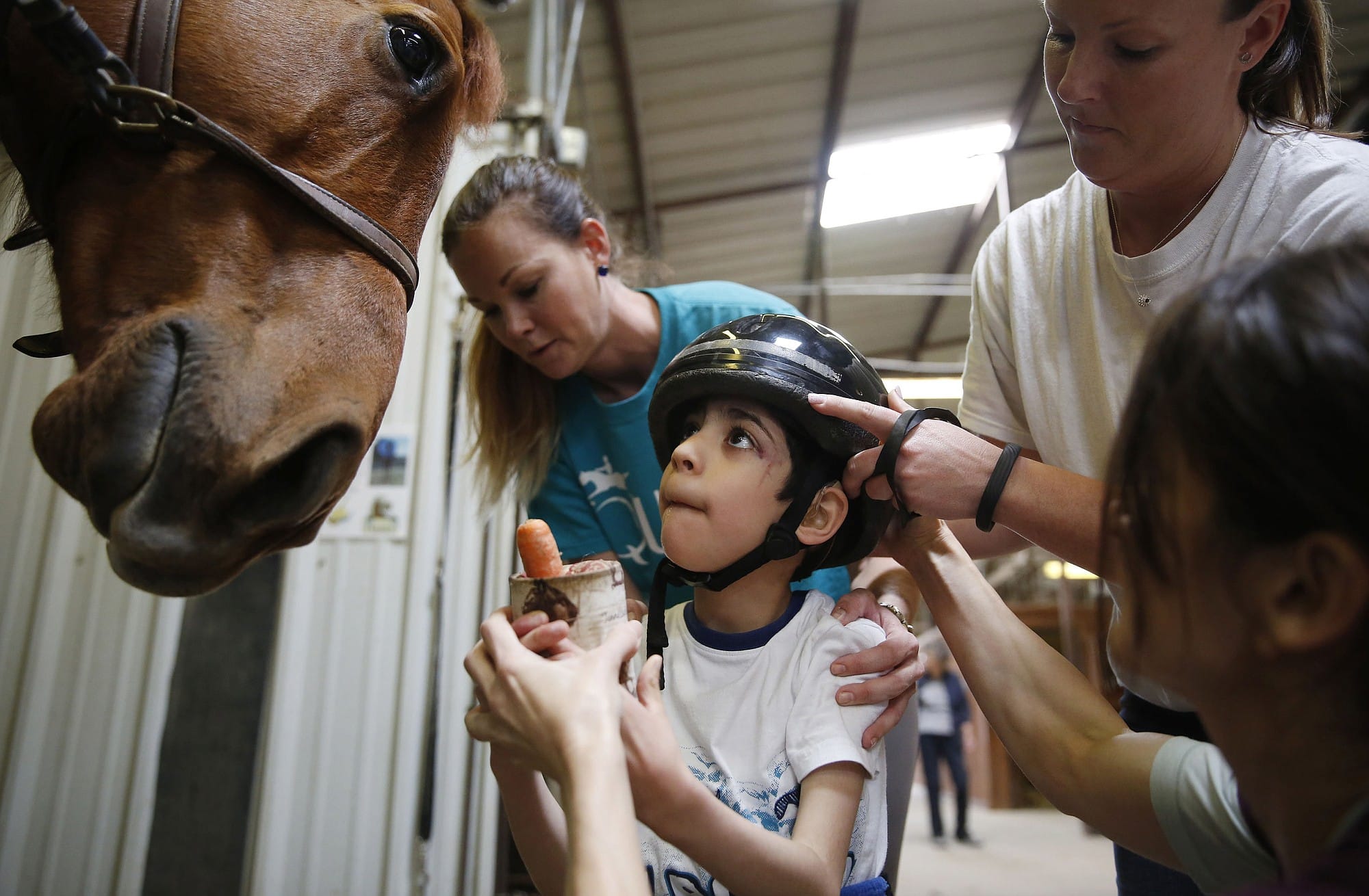 Clockwise from top left, Christa Collum, Megan Fishel, and therapist Kristi Immitt assist Jonathan Lopez, 7, of Rockwall, Texas, who has cerebral palsy, in feeding Patron a carrot during his hippotherapy session at Equest on March 31, 2015 in Rowlett, Texas. Lopez has been attending Equest for one year.