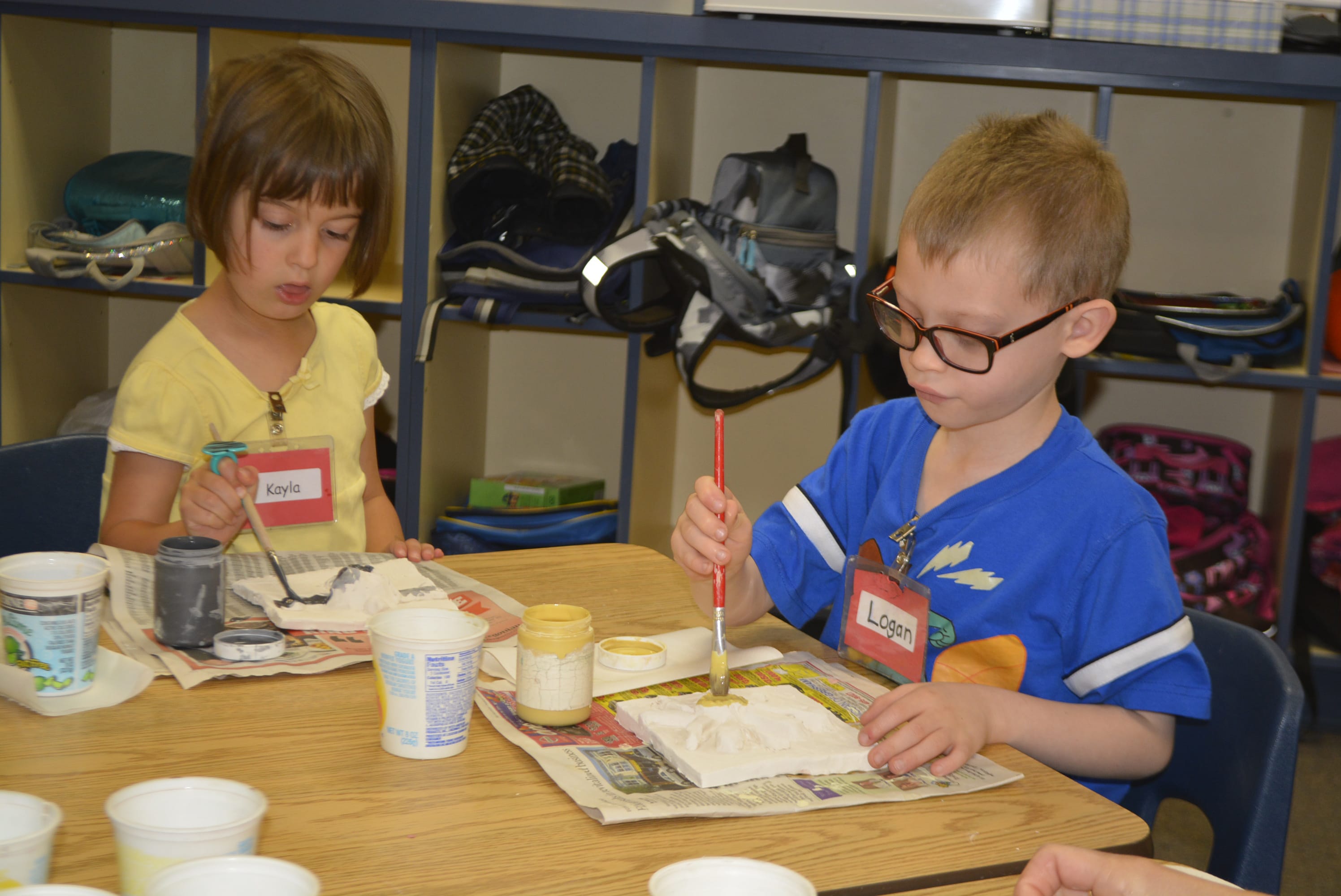 Kindergarteners Kayla Ruth (left) and Logan Jarvis apply paint to their clay tiles during the Artist in Residence program at Gause Elementary School.