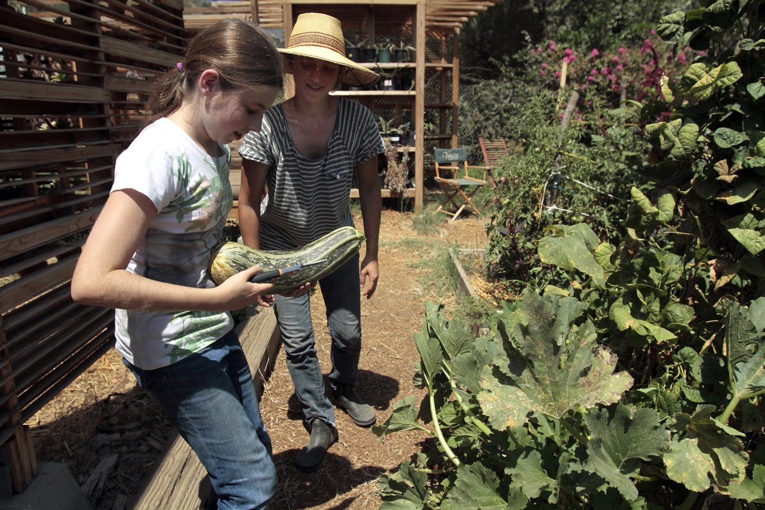 Macy, left, picks a large zucchini as teacher Faye Barry looks on at Taking the Reins in the Atwater Village neighborhood of Los Angeles.
