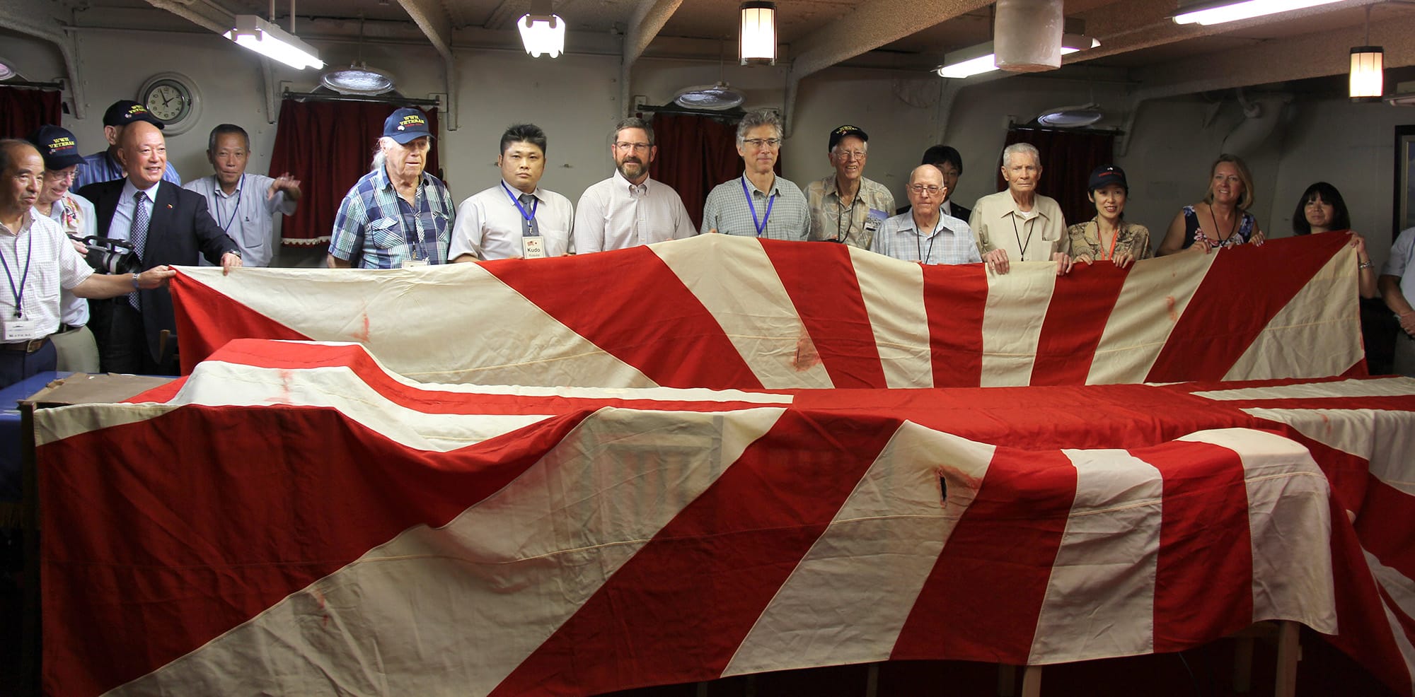 A group of visitors from the Northwest and members of a Japanese historical society unfold a flag that once flew from the Japanese battleship Asahi. An American Marine took it as a war trophy after World War II.