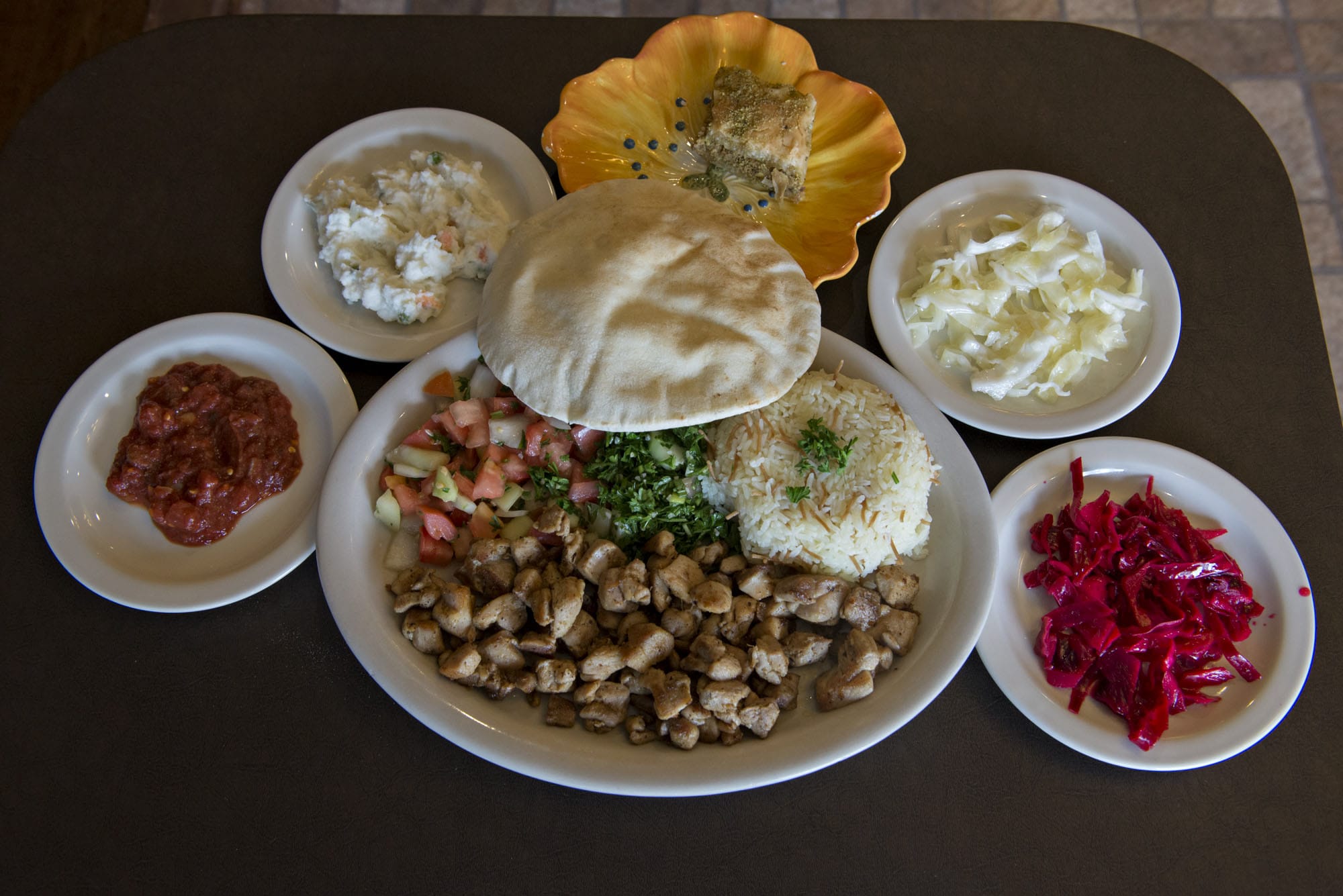 A chicken shawarma dinner, center, is served at the Pita House in Battle Ground along with house spicy sauce, clockwise from bottom left, house potato salad, pistachio baklava, green cabbage and red cabbage.